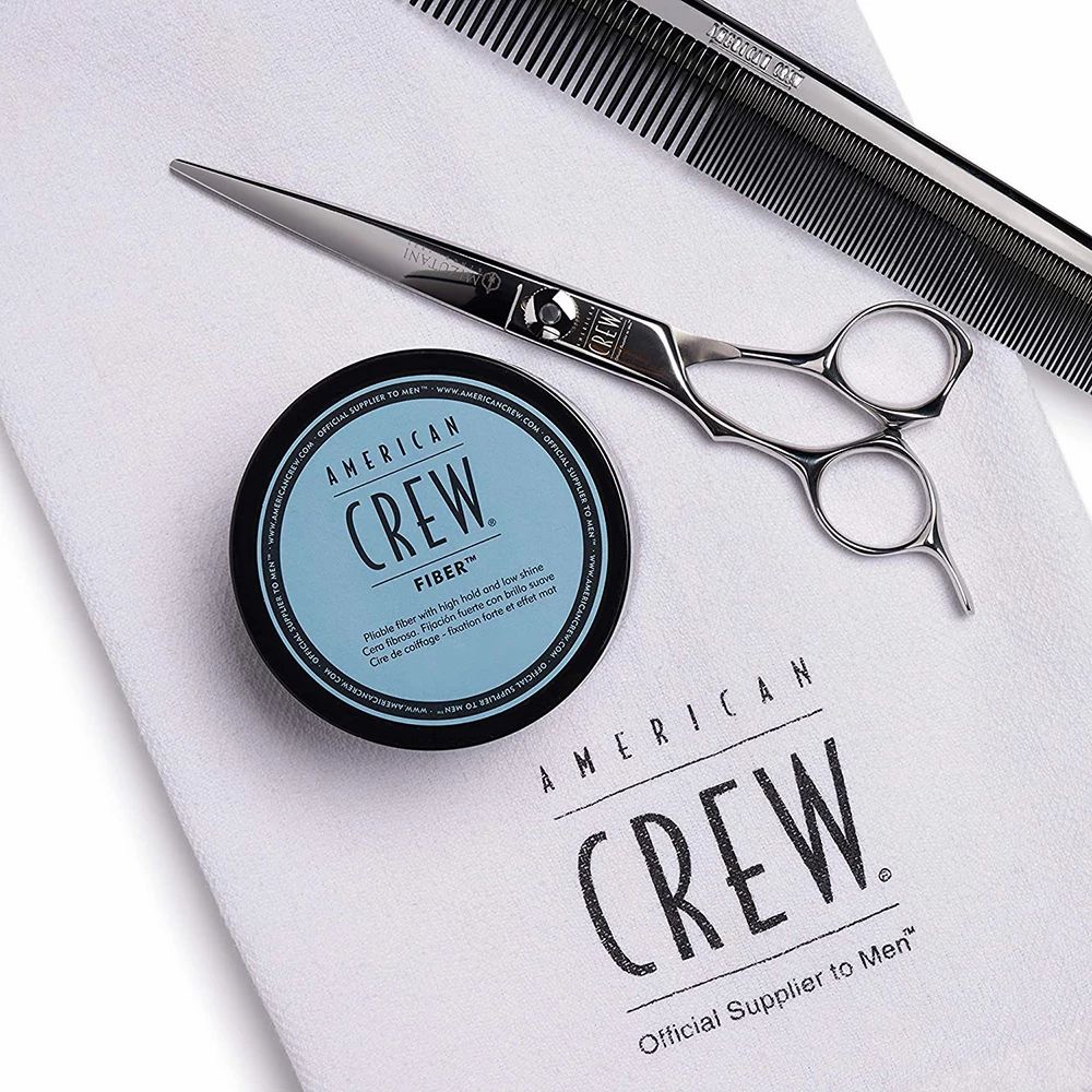 Dose, Schere und Kamm auf Handtuch. Dose: AMERICAN CREW FIBER. Schere: Metall. Kamm: Metall. Handtuch mit Logo.