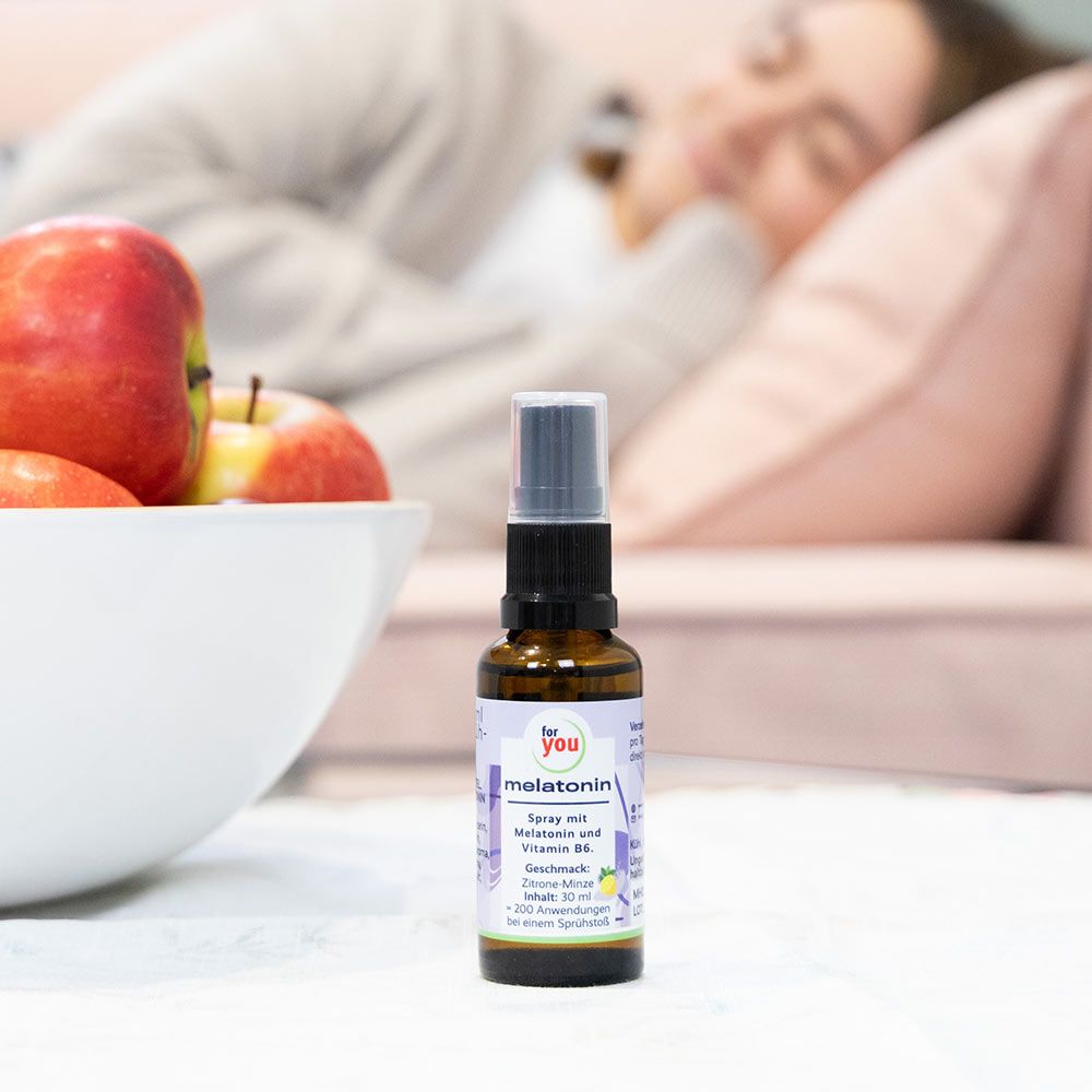 Melatonin Spray Flasche neben einer Schüssel Äpfel und einer schlafenden Person.