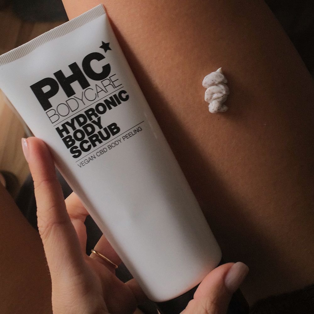 Weiße Tube mit schwarzer Schrift: PHC Bodycare Hydronic Body Scrub. Daneben ein Klecks des Scrubs auf der Haut. Vegan CBD Body Peeling.