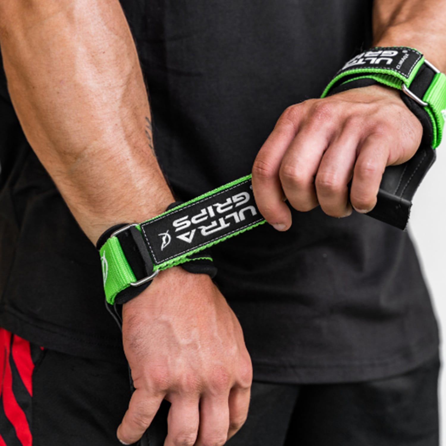 Zwei Hände mit Ultra-Grips. Grünes Band mit "ULTRA GRIPS"-Schriftzug. Person trägt schwarzes Shirt.