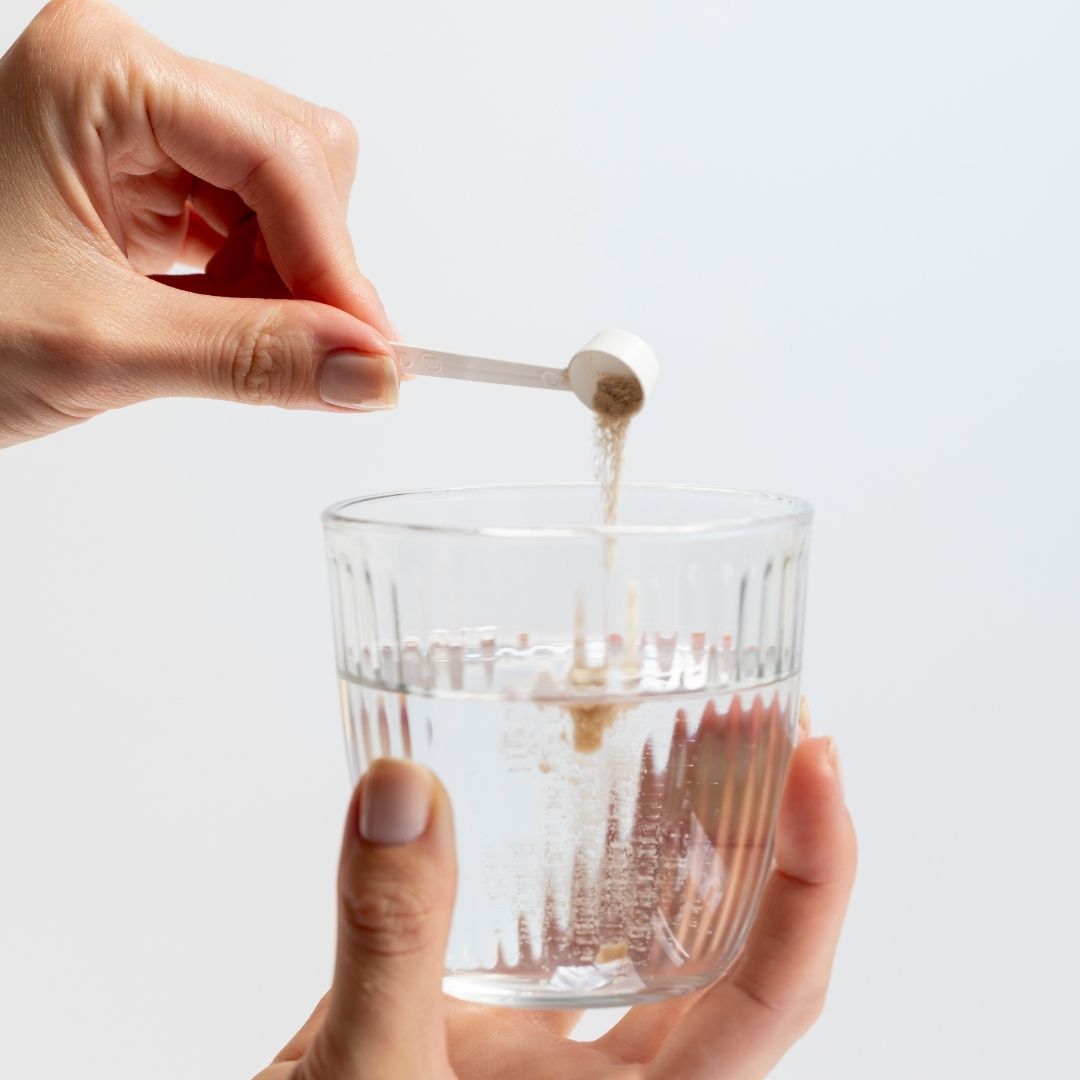 Pulver wird mit einem Löffel in ein Glas Wasser gegeben.