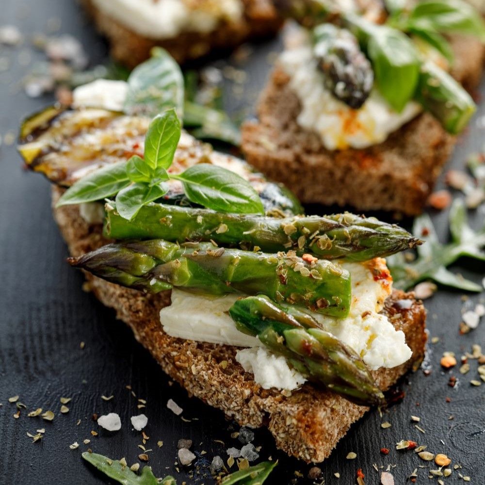 Geröstetes Brot mit Spargel, Käse und Basilikum. Nahaufnahme. Dunkler Untergrund. Gewürze verstreut.