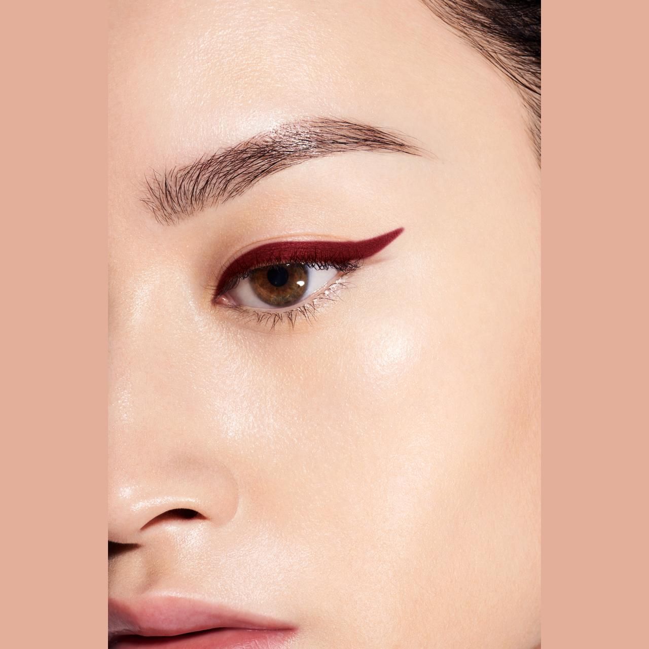 Auge mit dunkelrotem Eyeliner. Hautton hell. Braue definiert. Hintergrund einfarbig.