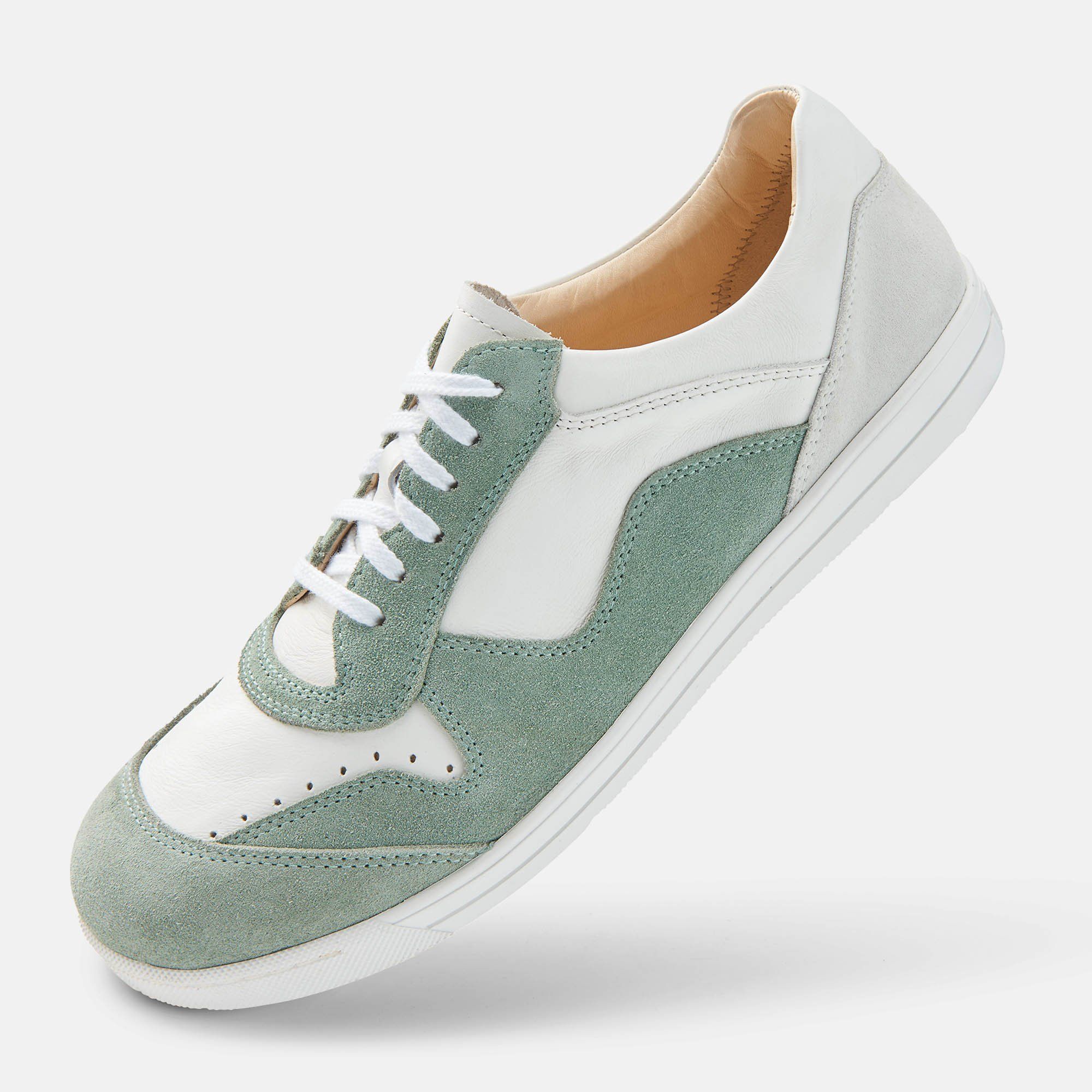 Ein weißer und mintfarbener Schnürschuh. Obermaterial aus Leder und Wildleder. Weiße Schnürsenkel. Weiße Sohle. Schuh schräg.