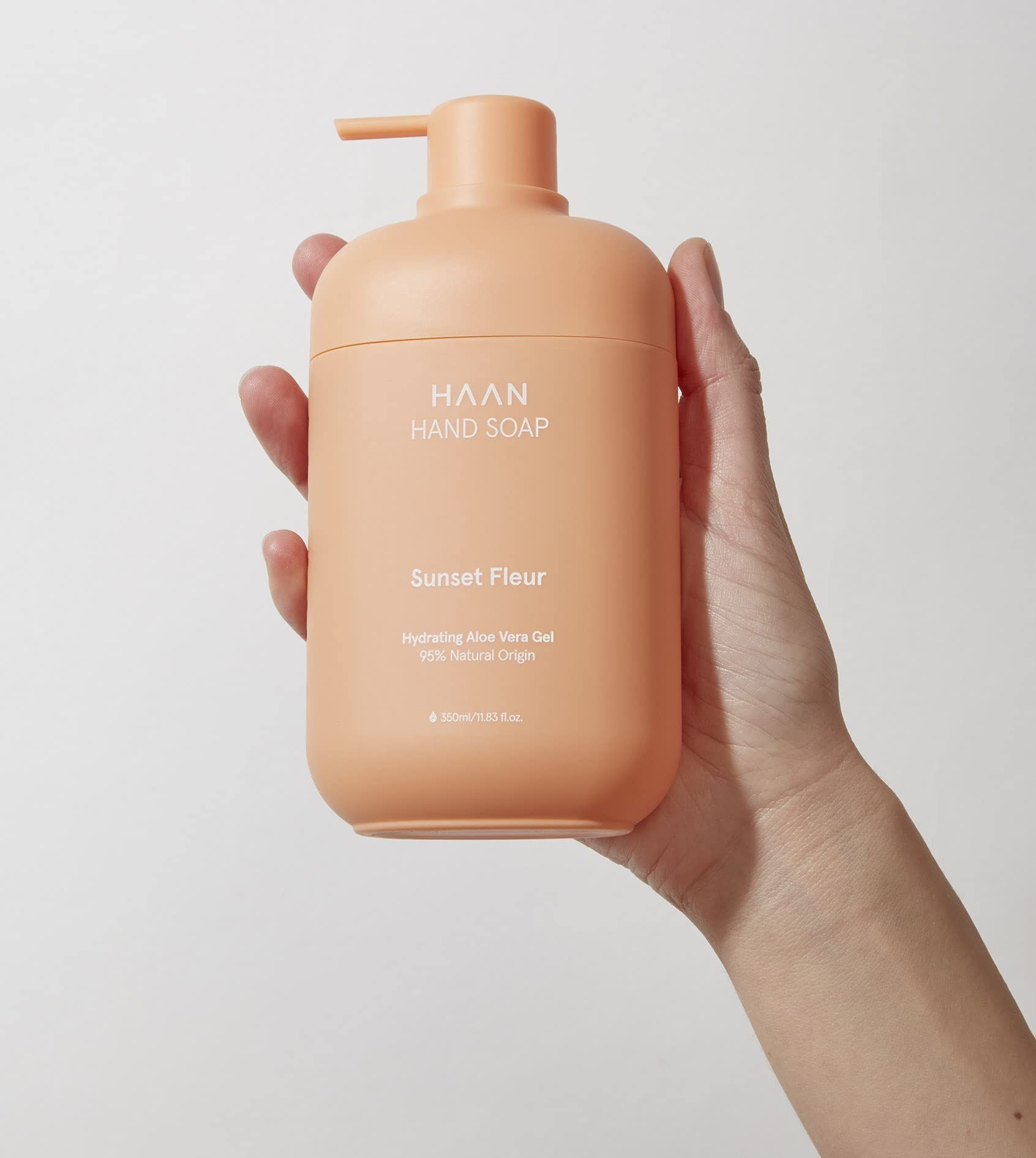 Hand hält orangefarbene Handseife mit Pumpkopf. Beschriftung: HAAN Hand Soap, Sunset Fleur, Hydrating Aloe Vera Gel, 98% Natural Origin.