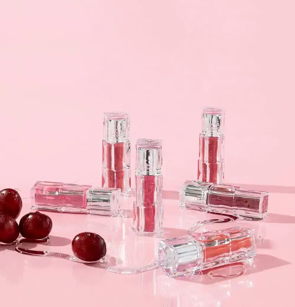 Mehrere transparente Lippenstifte mit silbernen Kappen auf rosa Untergrund, mit roten Beeren.