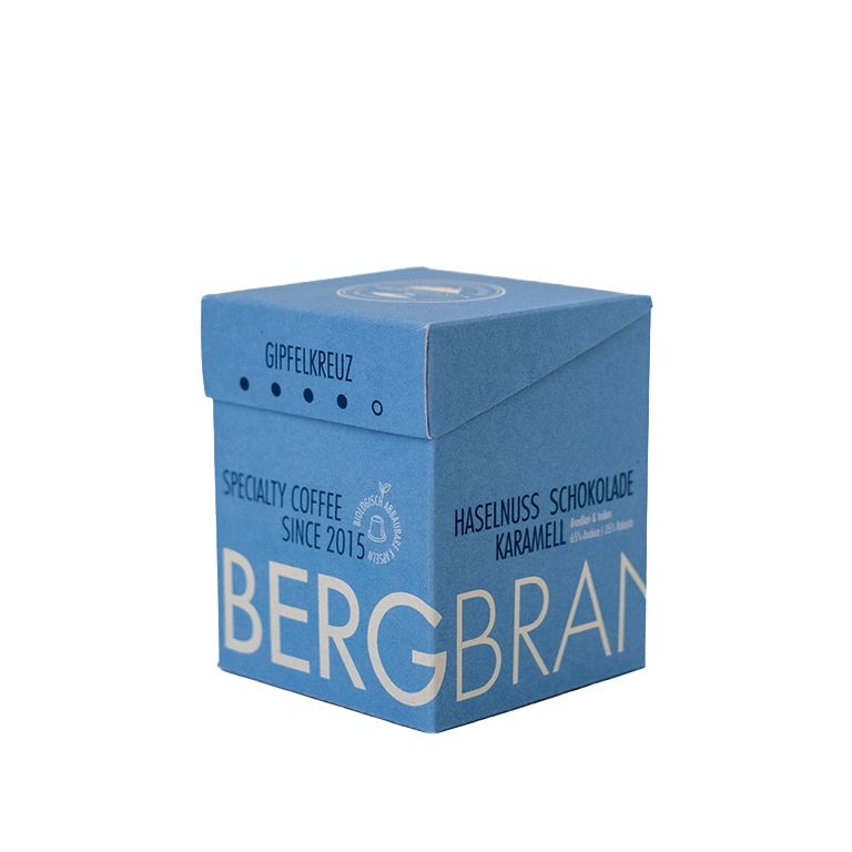 Blaue Box mit BERGBRAND-Logo. Text: Gipfelkreuz, Specialty Coffee, Haselnuss Schokolade.
