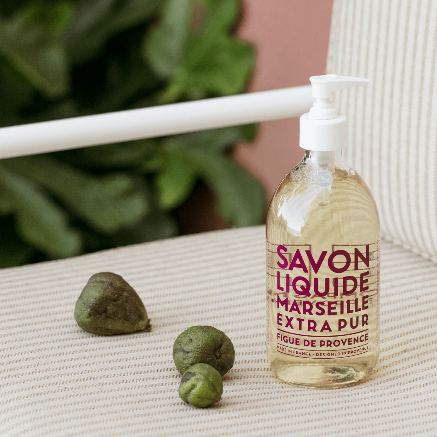 Flüssigseife mit Spender neben Feigen auf einem Stuhl. Aufschrift SAVON LIQUIDE MARSEILLE EXTRA PUR Figuier de Provence.