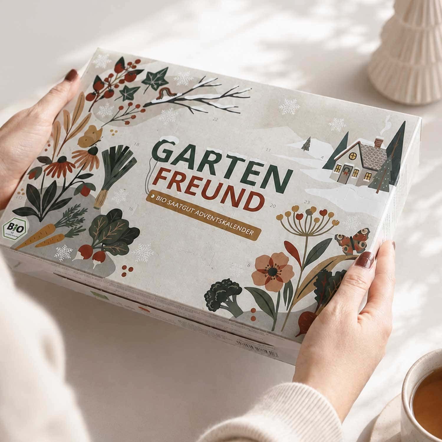 Person hält den BIO Saatgut Adventskalender "Garten Freund" mit winterlicher Dekoration.