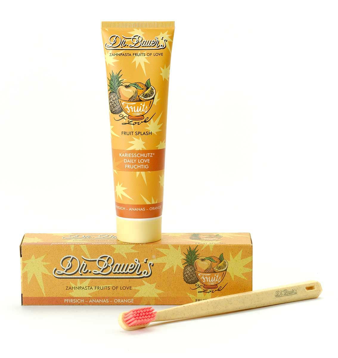 Zahnpasta-Tube, Schachtel und Zahnbürste. Tube und Schachtel mit Produktnamen und Frucht-Illustrationen. Zahnbürste aus Holz.