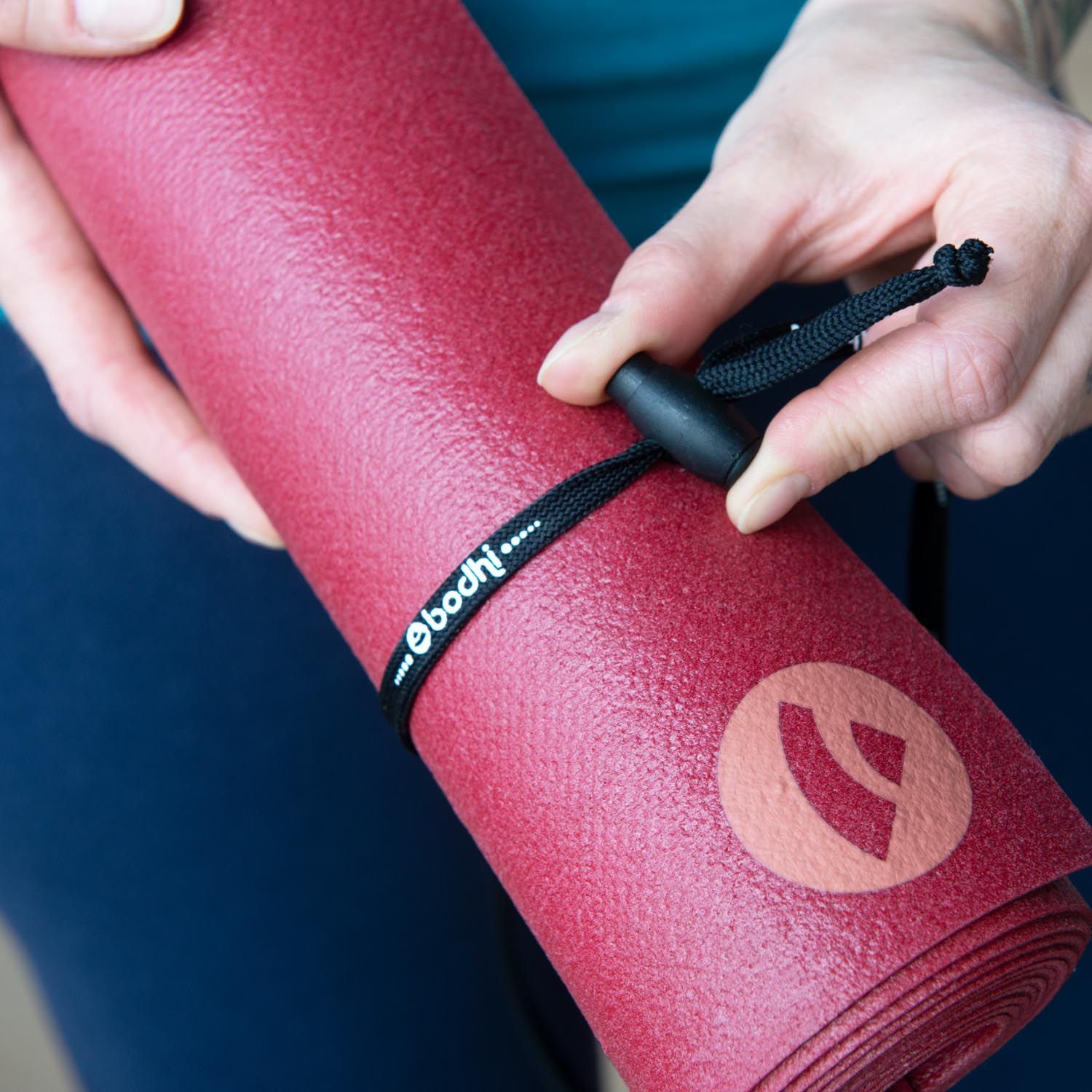 Person hält gerollte rote Yogamatte mit schwarzem Trageband. Band mit "bodhi"-Schriftzug.
