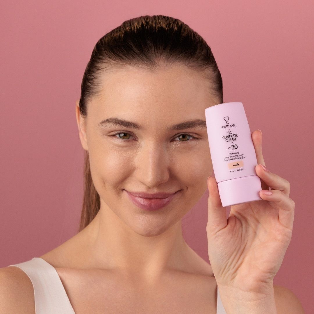 Frau hält eine Tube YOUTH LAB CC Complete Cream Vanilla. Rosa Tube mit Produktinformationen.