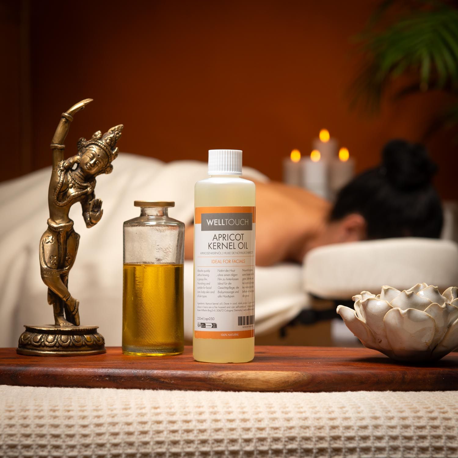 Welltouch Aprikosenkernöl-Flasche und Glasflasche mit Öl auf Holztablett. Frau erhält Massage. Dekoration.