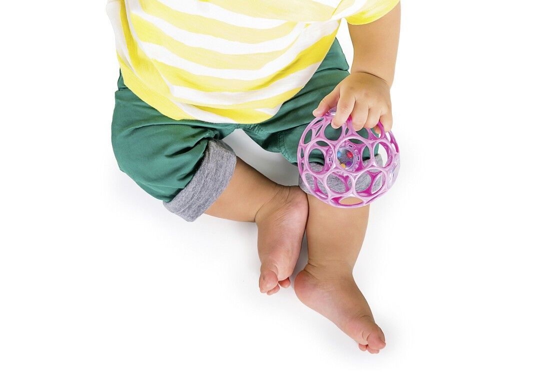 Ein Baby hält eine rosa Rassel. Das Baby trägt ein gelb-weiß gestreiftes Shirt und grüne Shorts.