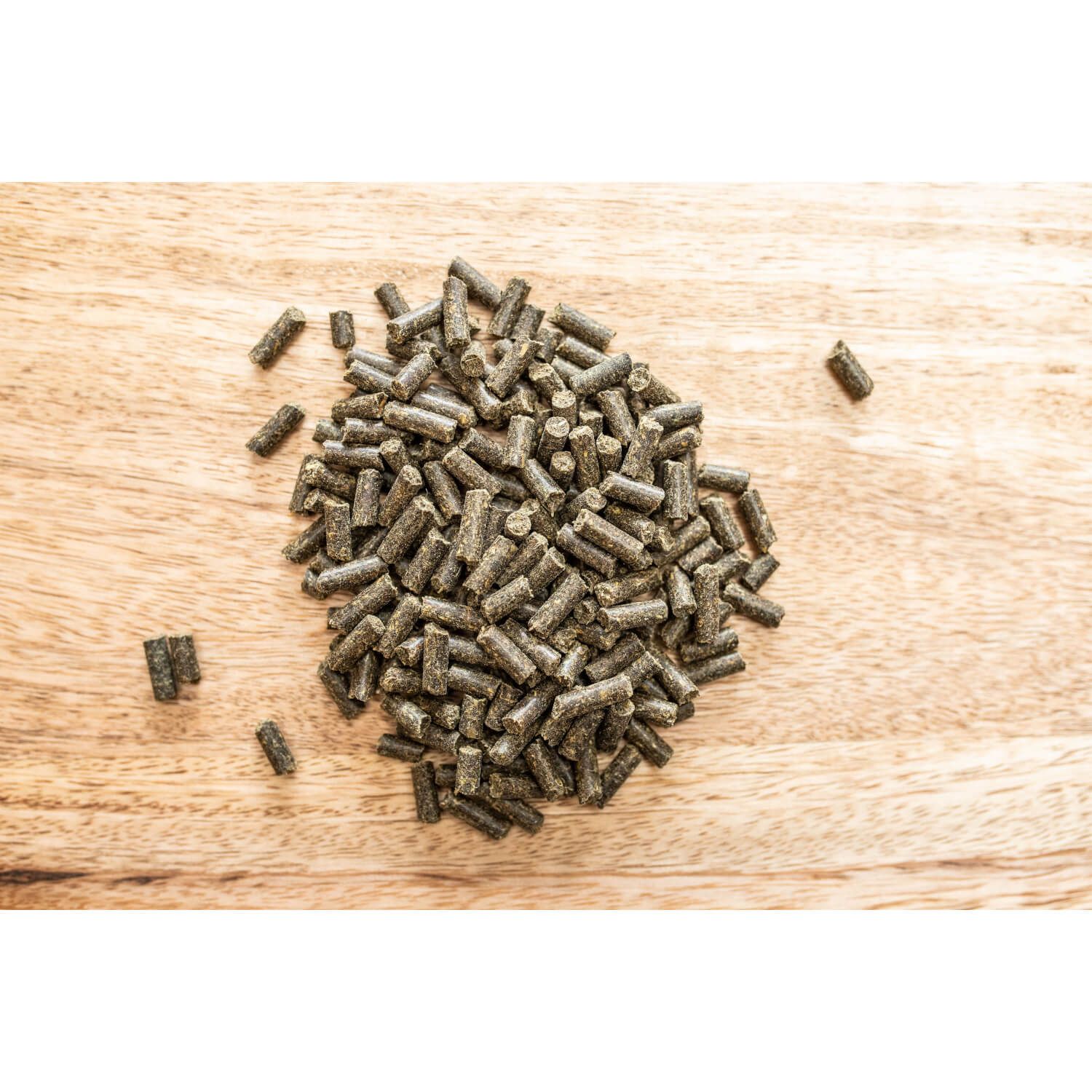 Haufen von kleinen, zylindrischen Pellets auf Holzuntergrund. Farbe: braun-grün.