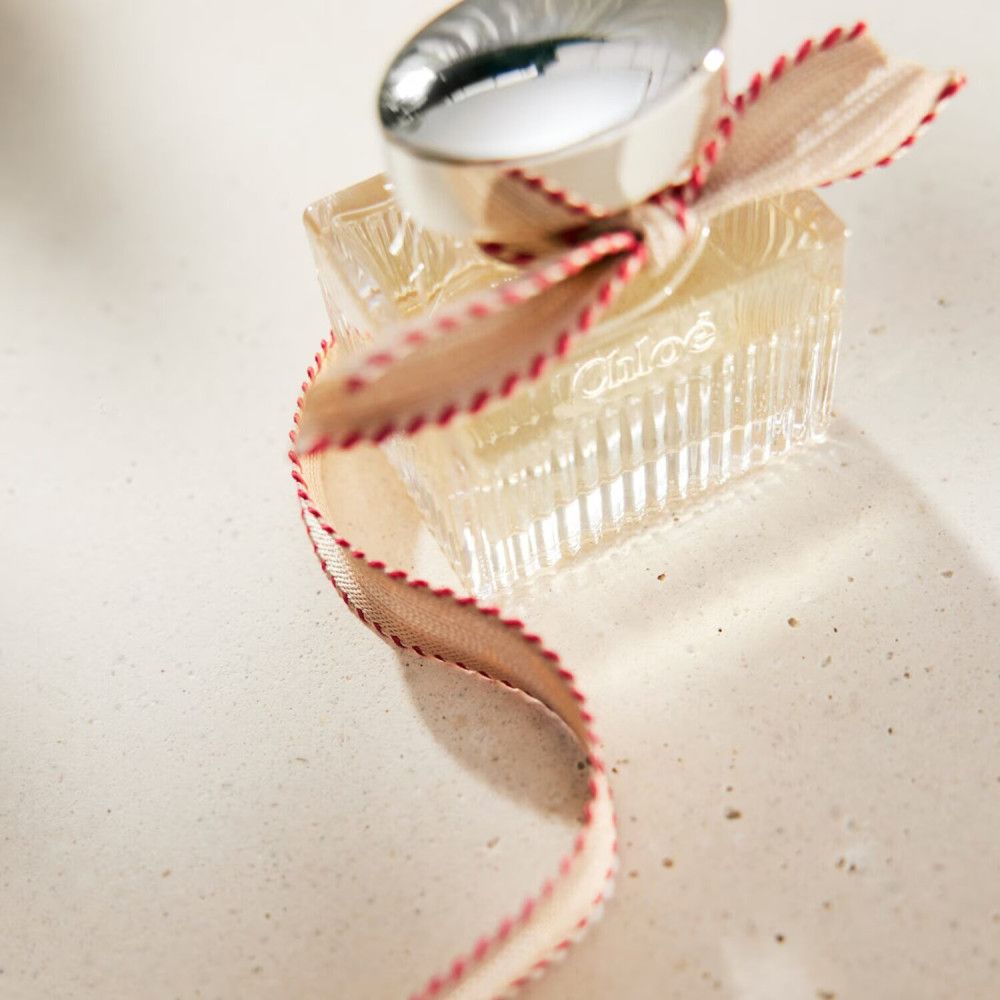 Glasflakon mit silbernem Deckel und Schleife. Der Flakon hat eine rechteckige Form. Der Markenname ist nicht sichtbar.