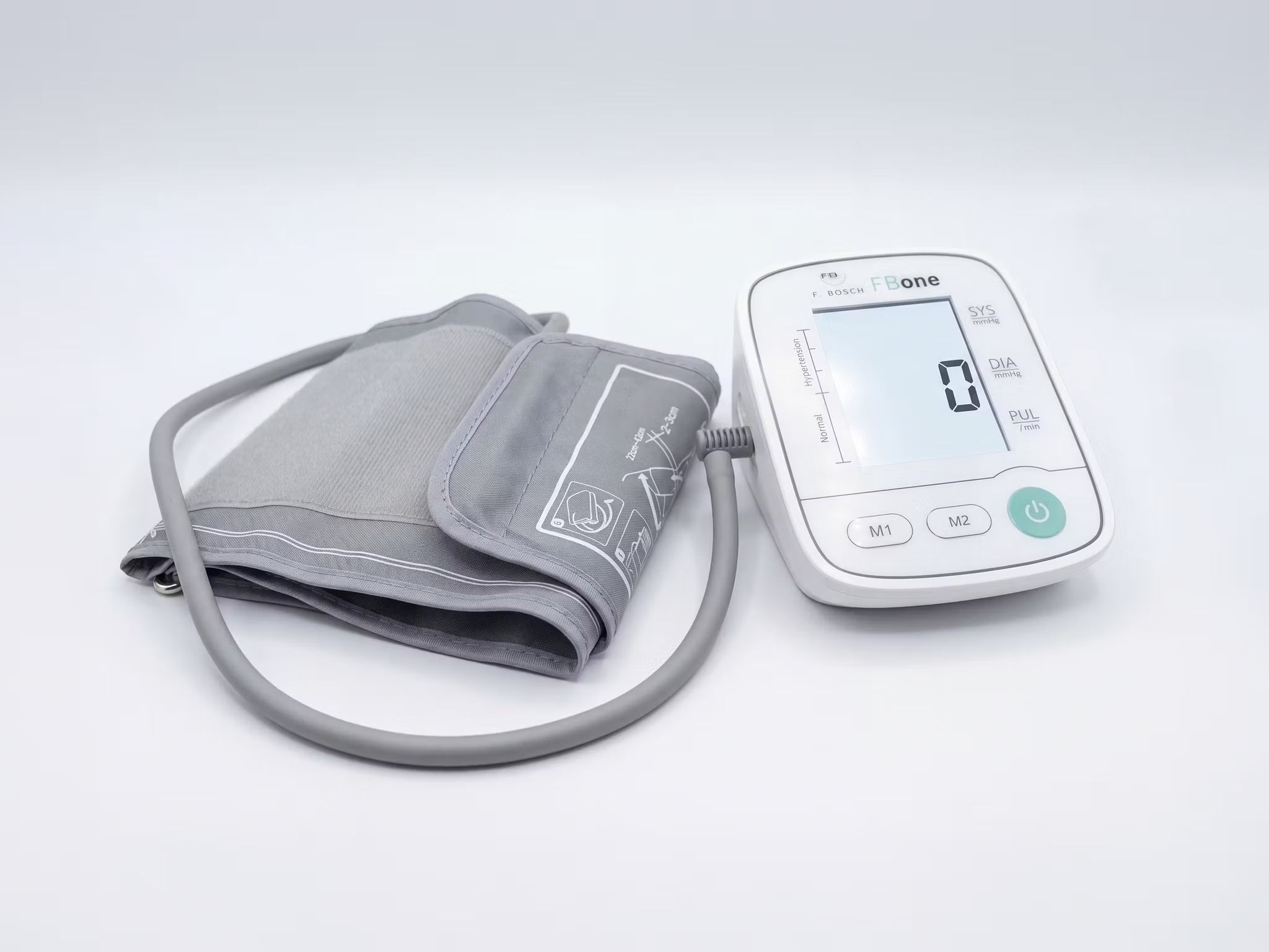 FBone Oberarm-Blutdruckmessgerät mit Manschette. Weißes Gerät mit digitalem Display und grauer Manschette.
