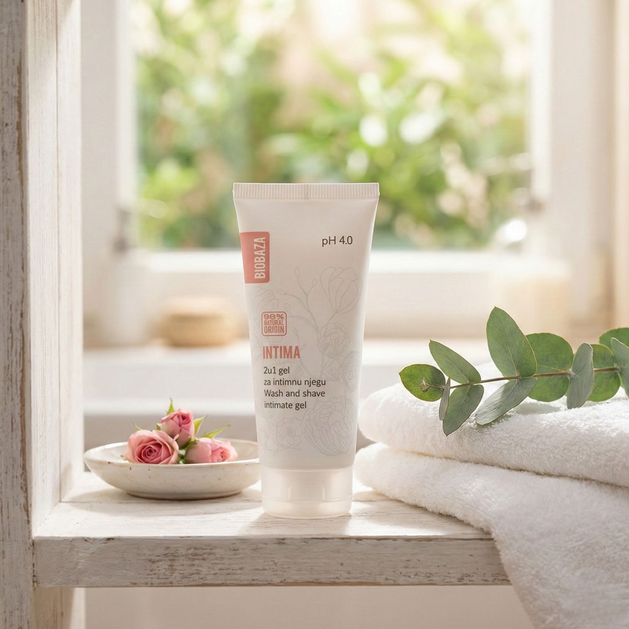 Weiß-rosa Tube Intim-Waschgel, pH 4.0. Auf Holzregal, neben Handtüchern und Rosen. Fenster im Hintergrund.