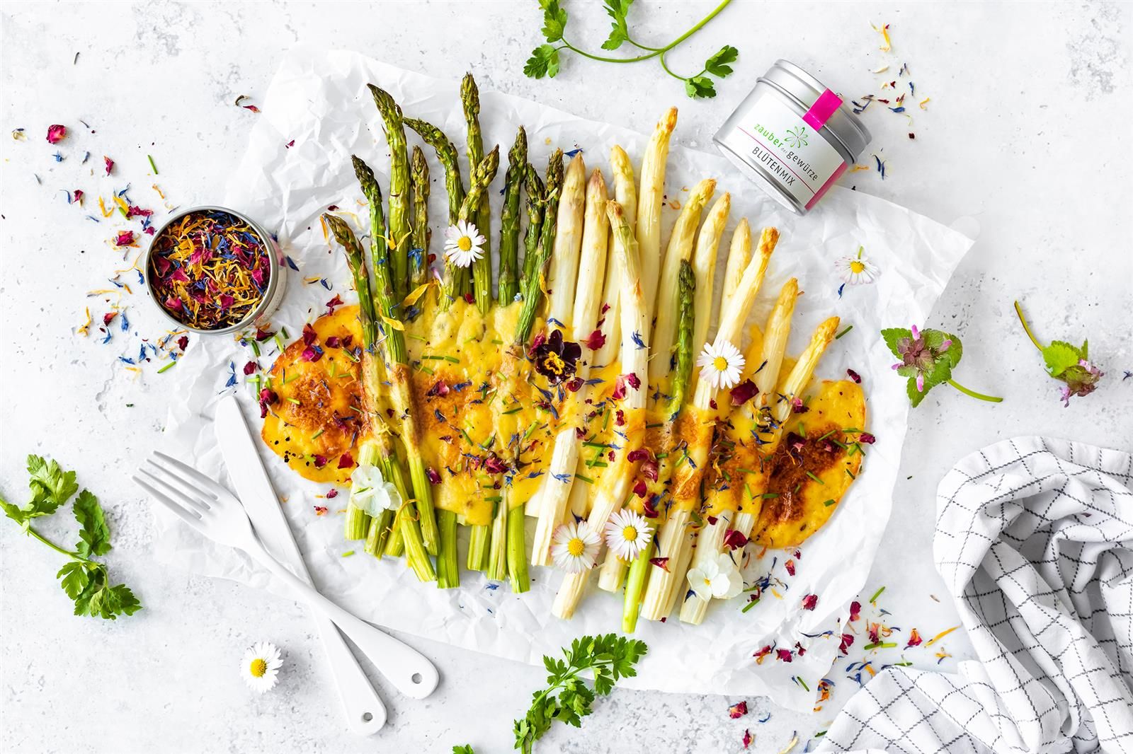 Spargelgericht mit Blüten und Kräutern. Dose Spargel Gewürz daneben. Auf Papier angerichtet.