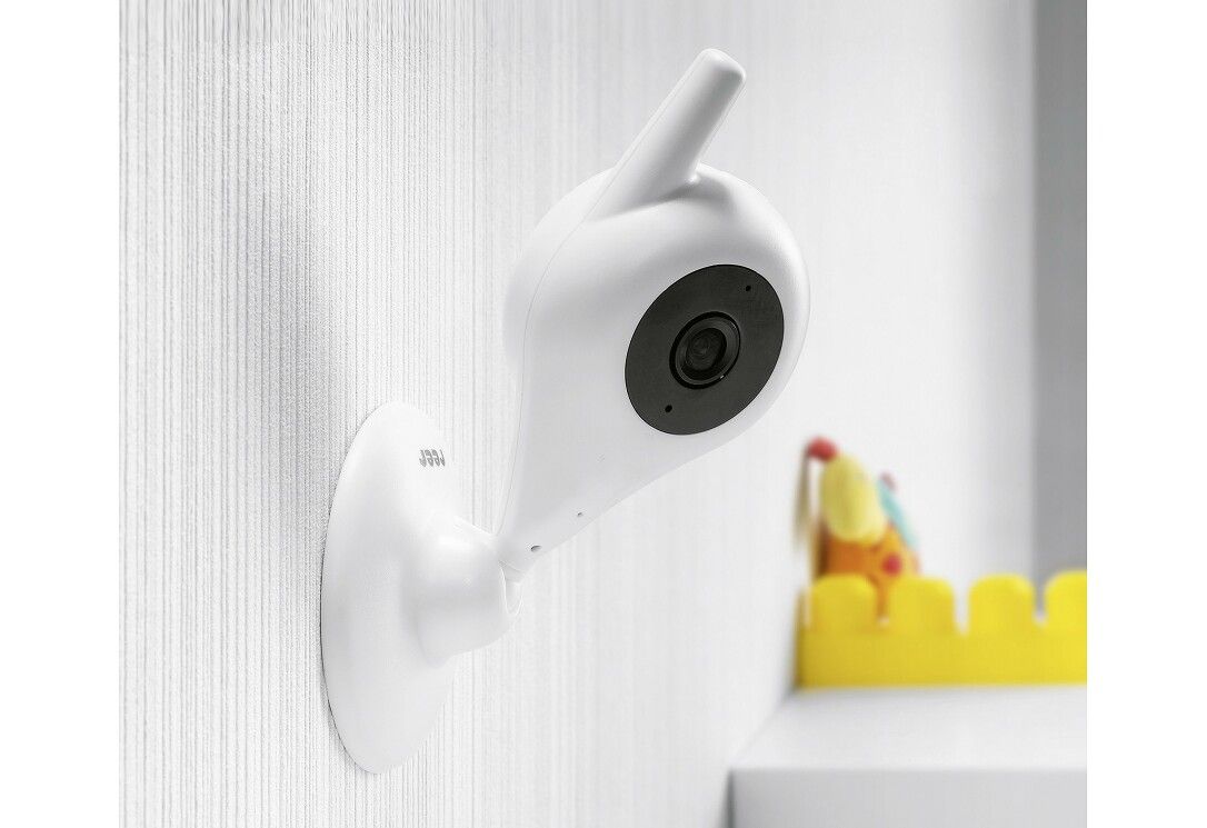 Weiße Babykamera an einer Wand befestigt. Die Kamera hat ein rundes Objektiv und eine Antenne. Gelbes Spielzeug im Hintergrund.