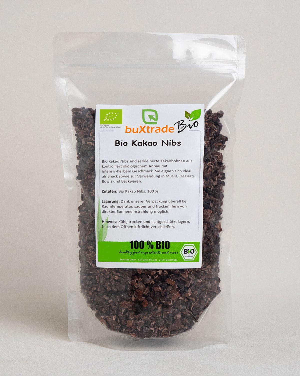 Bio Kakaonibs in einem Standbodenbeutel. Kleine weiße Würfel mit Kakaonibs und ein Holzschaufelchen sind daneben platziert.