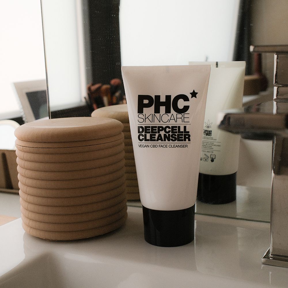 Weiße Tube mit schwarzem Deckel. Aufschrift: PHC Skincare Deepcell Cleanser. Steht auf einer Ablage.