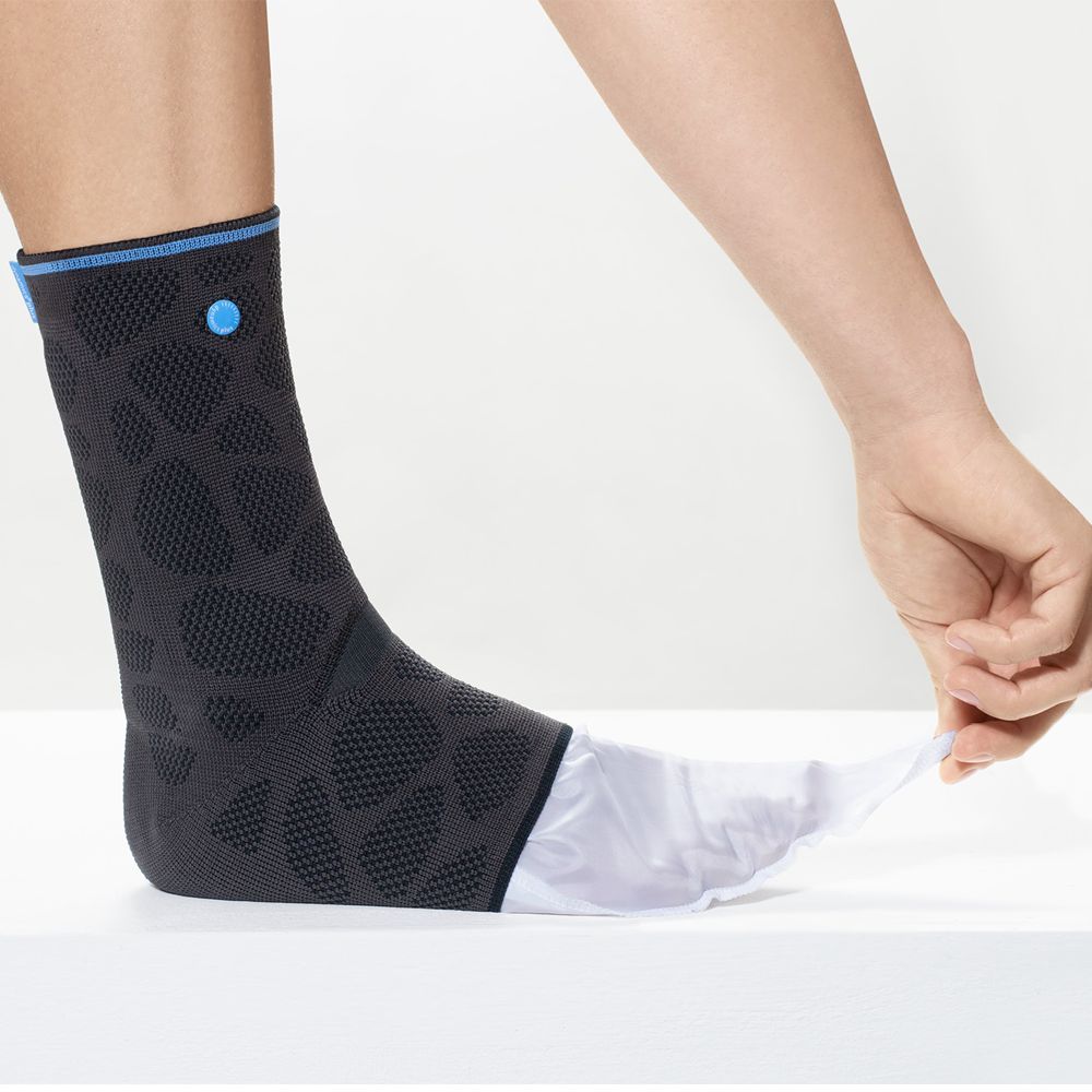 Person zieht weiße Hülle aus Achillessehnenbandage. Schwarz mit blauen Akzenten. Auf weißer Oberfläche.
