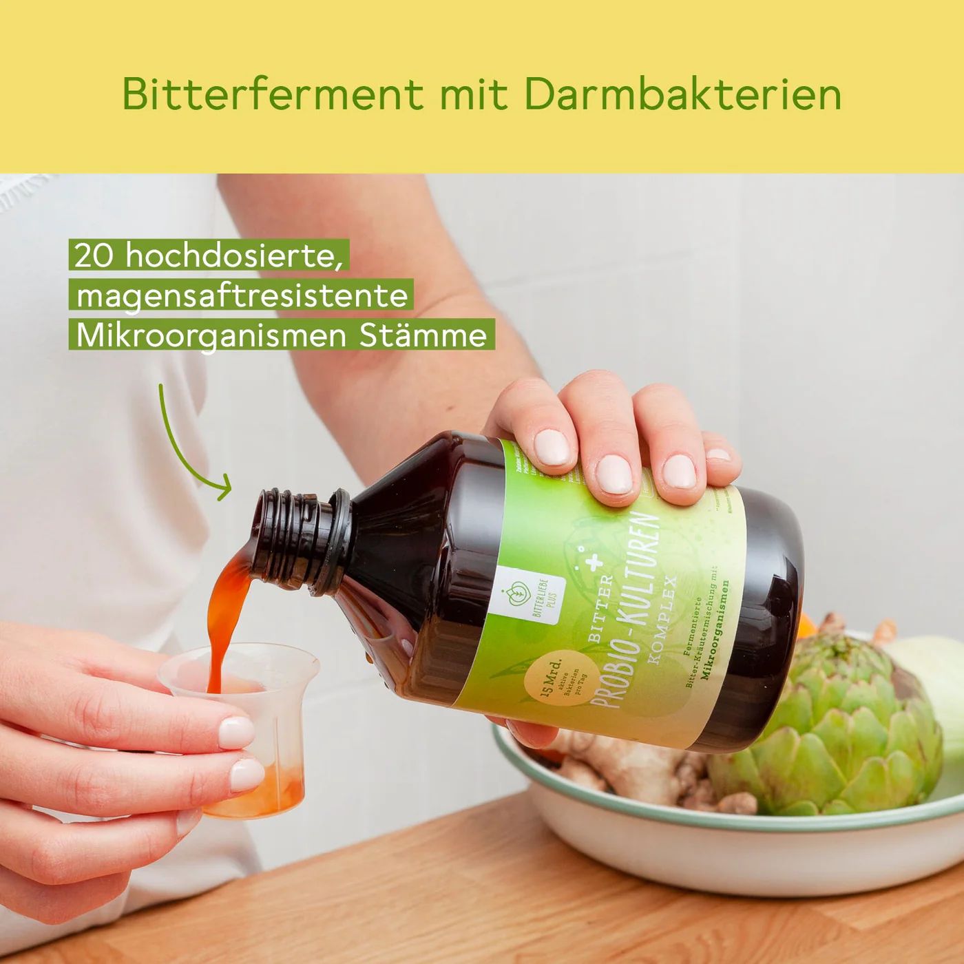 Person gießt Flüssigkeit aus einer Flasche in einen Messbecher. Aufschrift: Bitter Probio-Kulturen Komplex. Text: Bitterferment mit Darmbakterien. 20 hochdosierte Stämme.