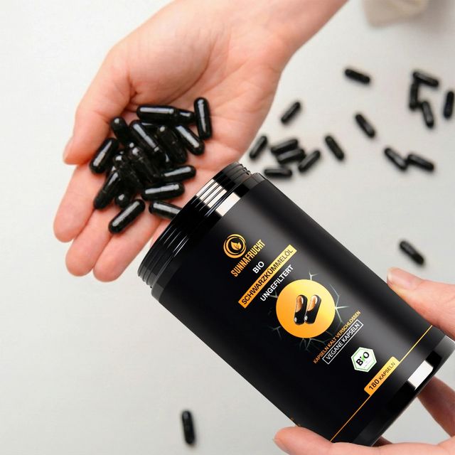 Hand schüttet Schwarzkümmelöl Kapseln aus Dose. Mehrere Kapseln in der Hand und auf der Oberfläche.