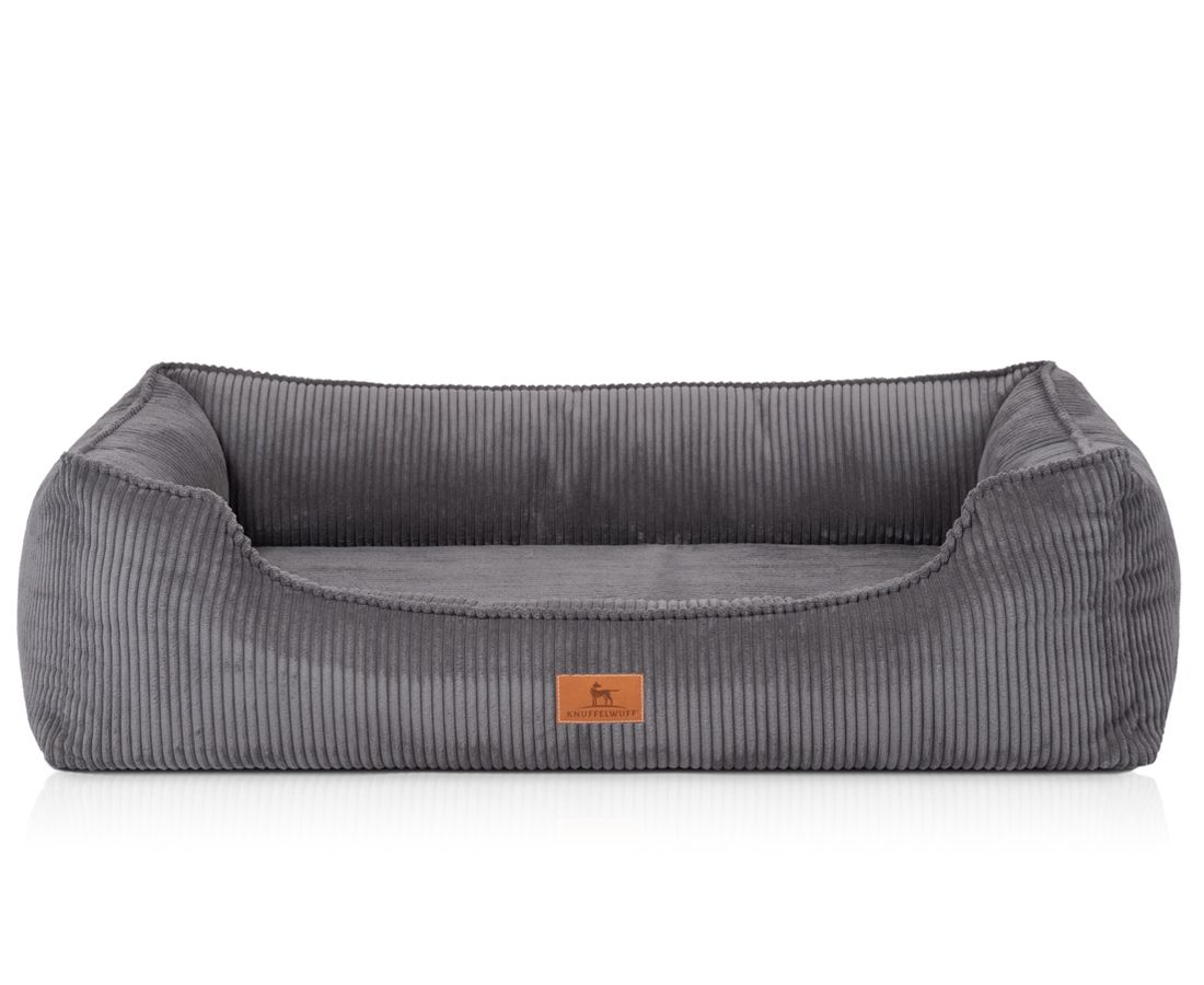 Graues orthopädisches Hundebett mit Cordstruktur. Rechteckige Form mit erhöhten Seiten. Braunes Label mit Logo.