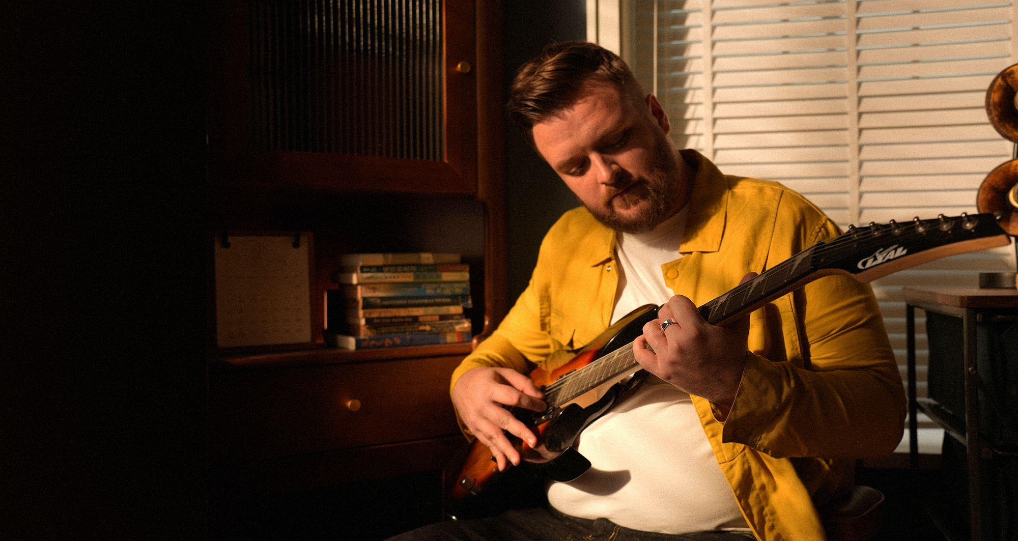 Mann spielt Gitarre mit goldenem Ring. Er sitzt in einem Raum.