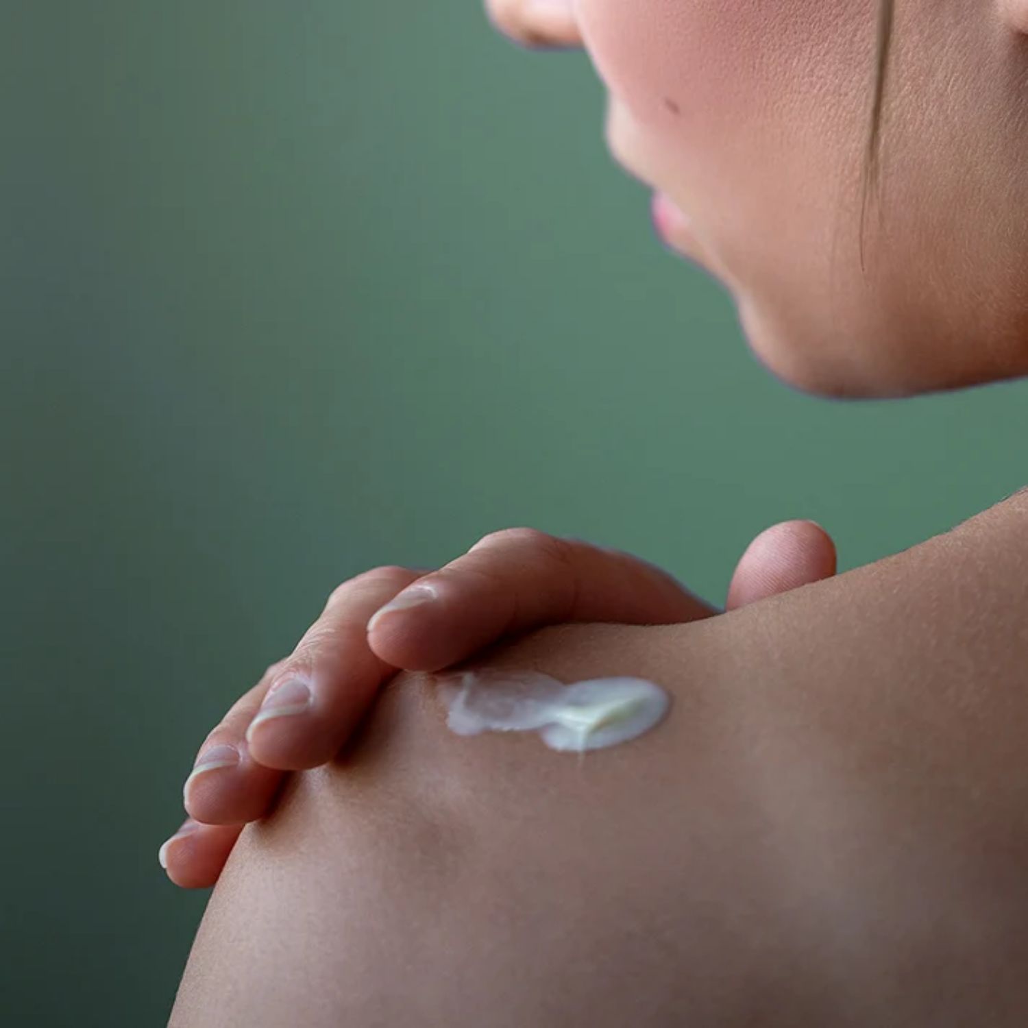 Eine Hand trägt eine kleine Menge weißer Lotion auf die Schulter einer Person auf.