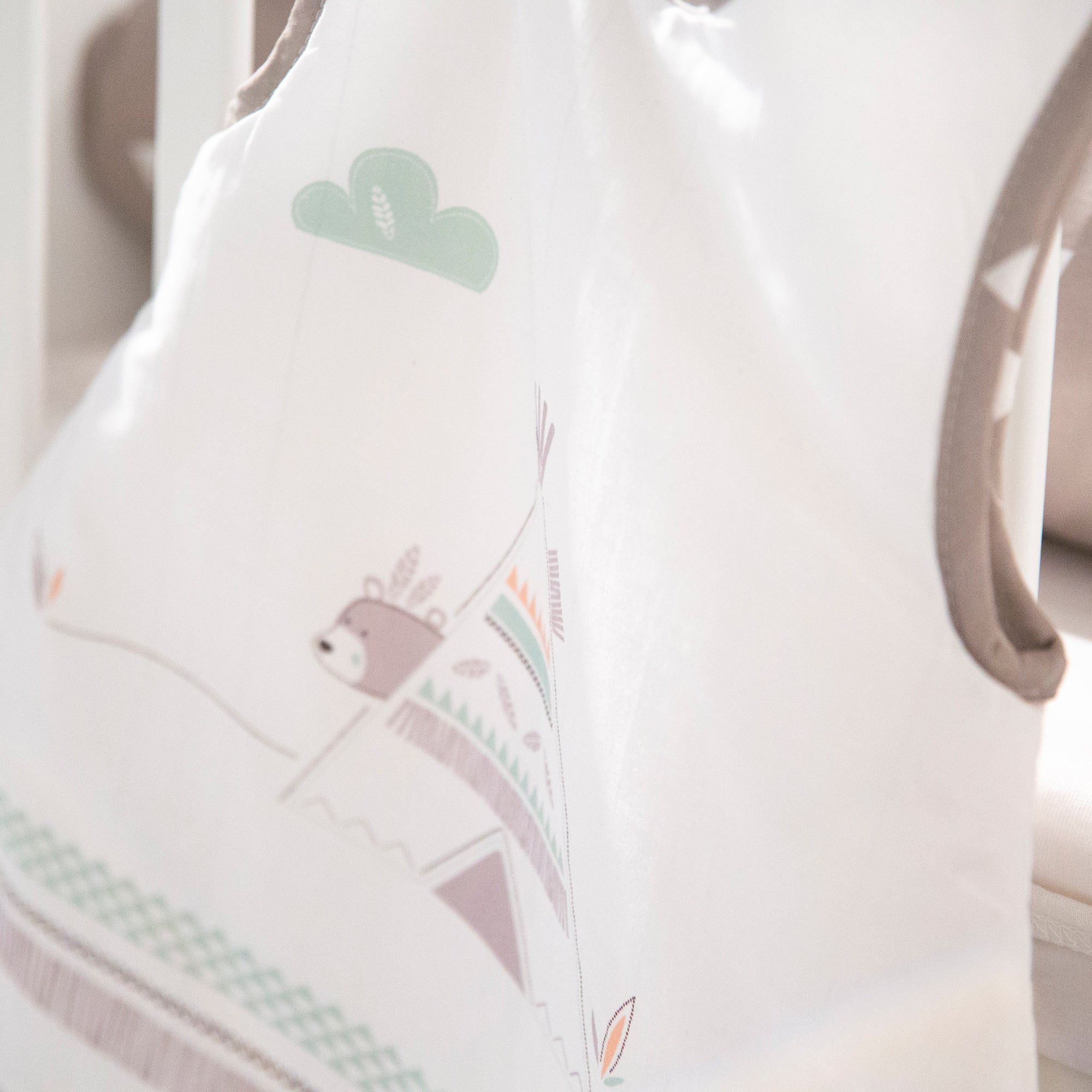 Babyschlafsack mit Bären- und Tipi-Motiv. Weiß mit braunen und grünen Akzenten. Detailansicht, teilweise im Kinderbett.
