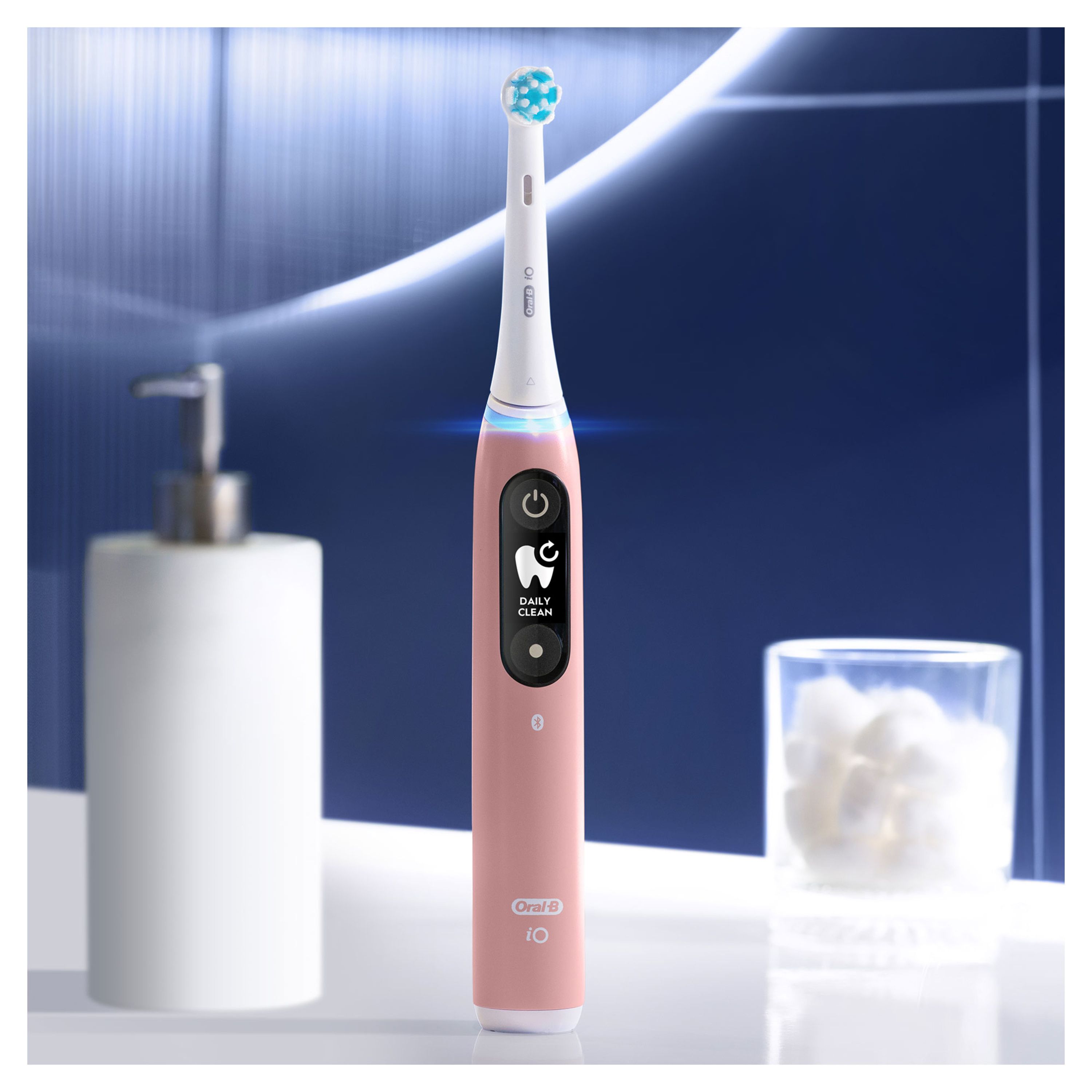 Pinke elektrische Zahnbürste mit digitalem Display. Steht neben Seifenspender und Glas mit Wattepads. Oral-B iO.