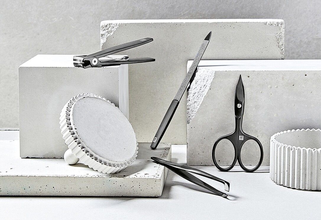 Verschiedene Maniküre-Werkzeuge, darunter ein Nagelknipser mit ZWILLING-Logo. Auf Betonblöcken platziert.