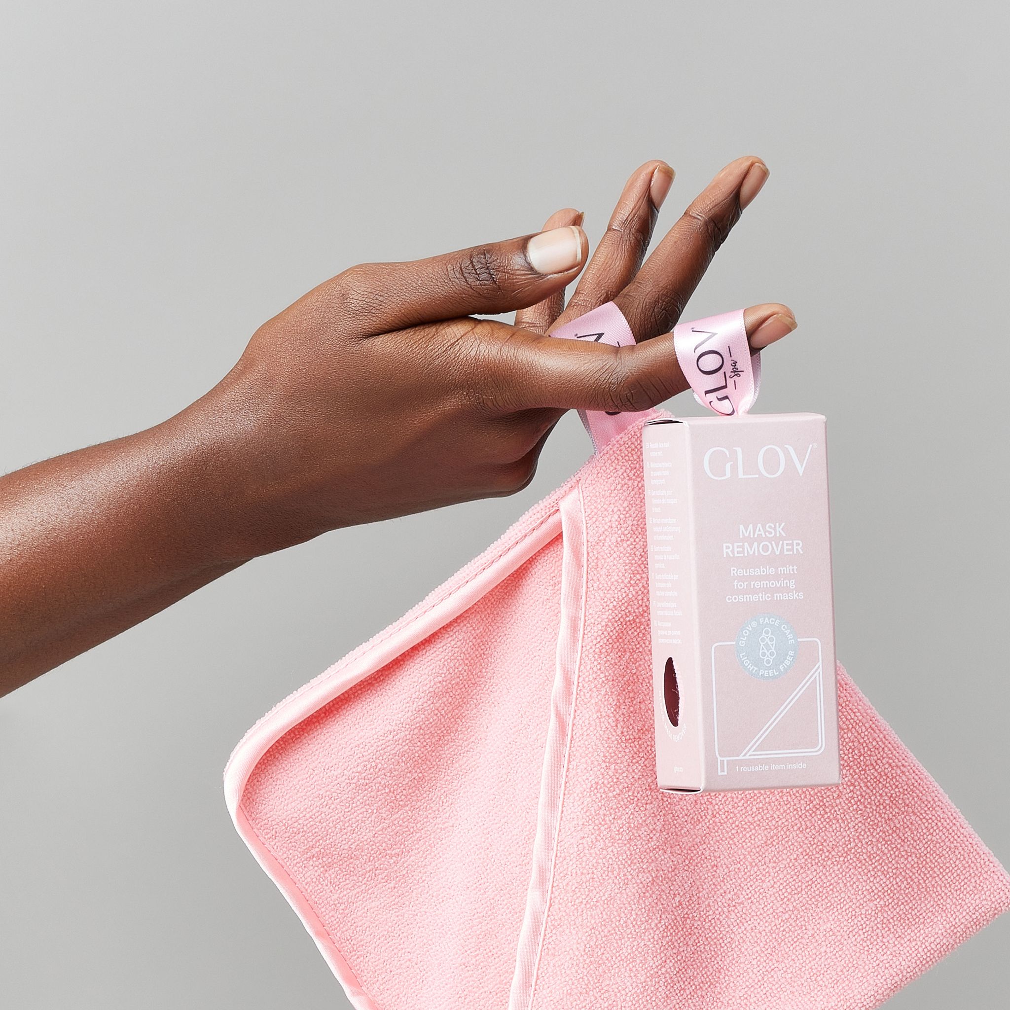 Eine Hand hält ein rosa Handtuch und eine kleine rosa Verpackung mit der Aufschrift "GLOV".
