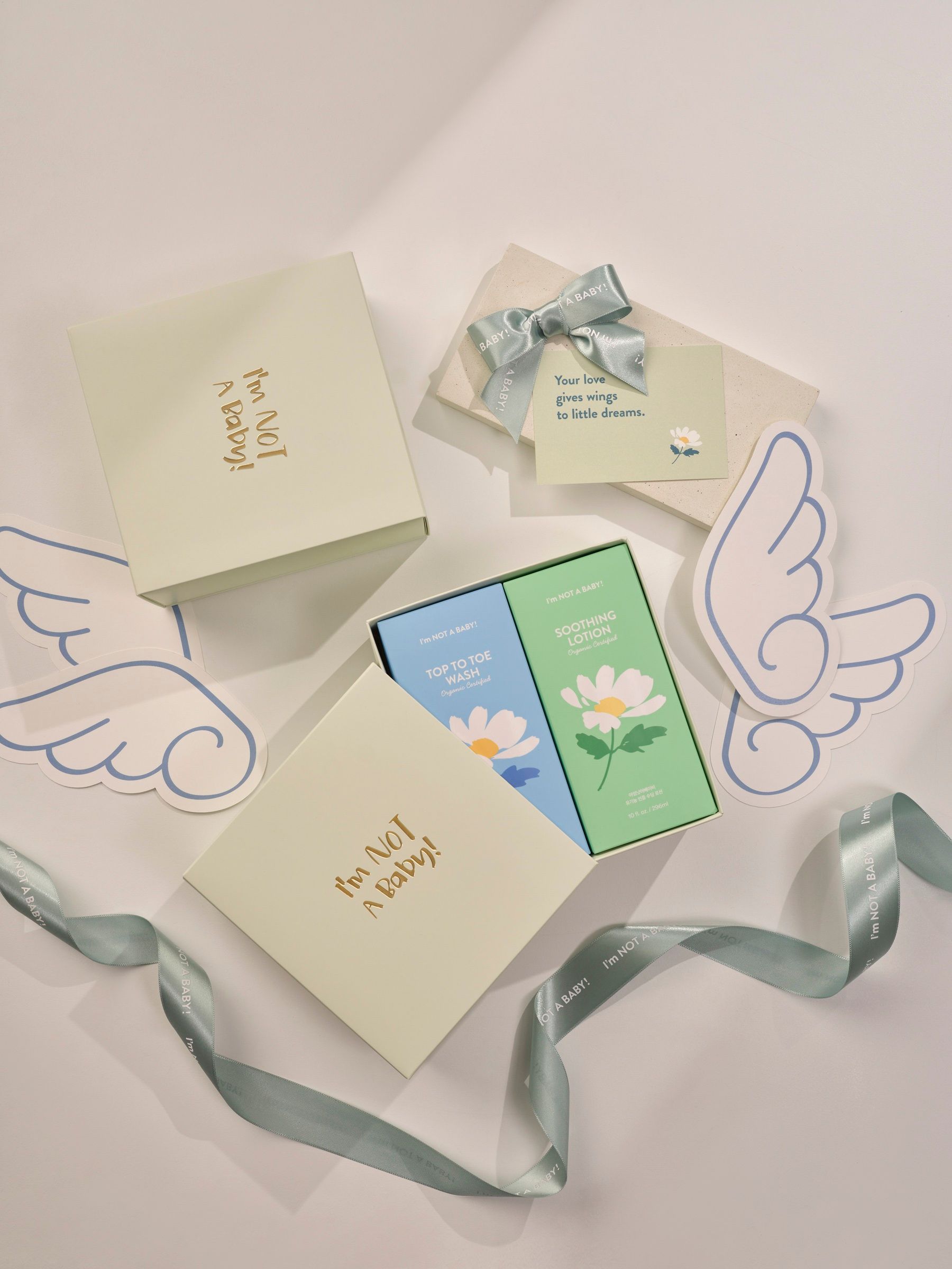 Geschenkboxen mit Aufschrift I'm NOT A BABY. Zwei Schachteln mit floralen Motiven. Dekorative Engelsflügel und Schleifen.