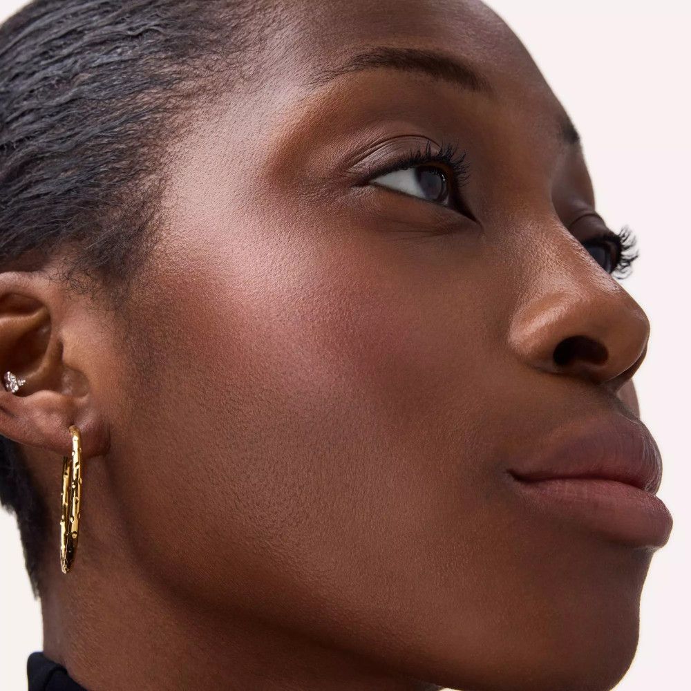 Nahaufnahme eines Gesichts mit Rouge auf den Wangen. Die Person trägt Ohrringe.