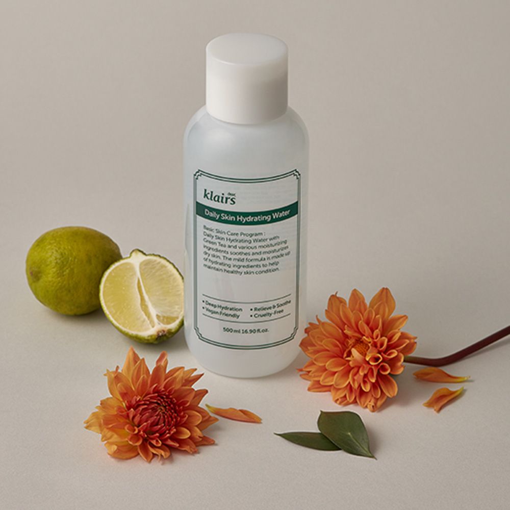 Weiße Flasche mit grünem Etikett, neben Limette und orangefarbenen Blüten. Text: klairs, Daily Skin Hydrating Water.