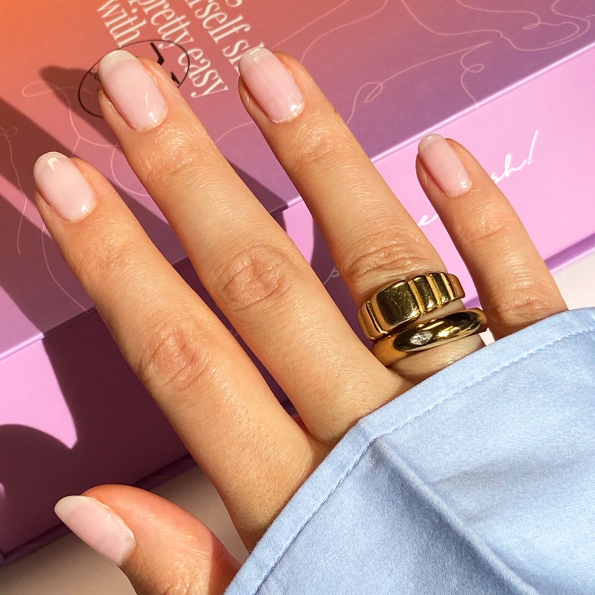 Hand mit lackierten Nägeln. Goldene Ringe. Helle Nagellackfarbe. Blauer Ärmel.