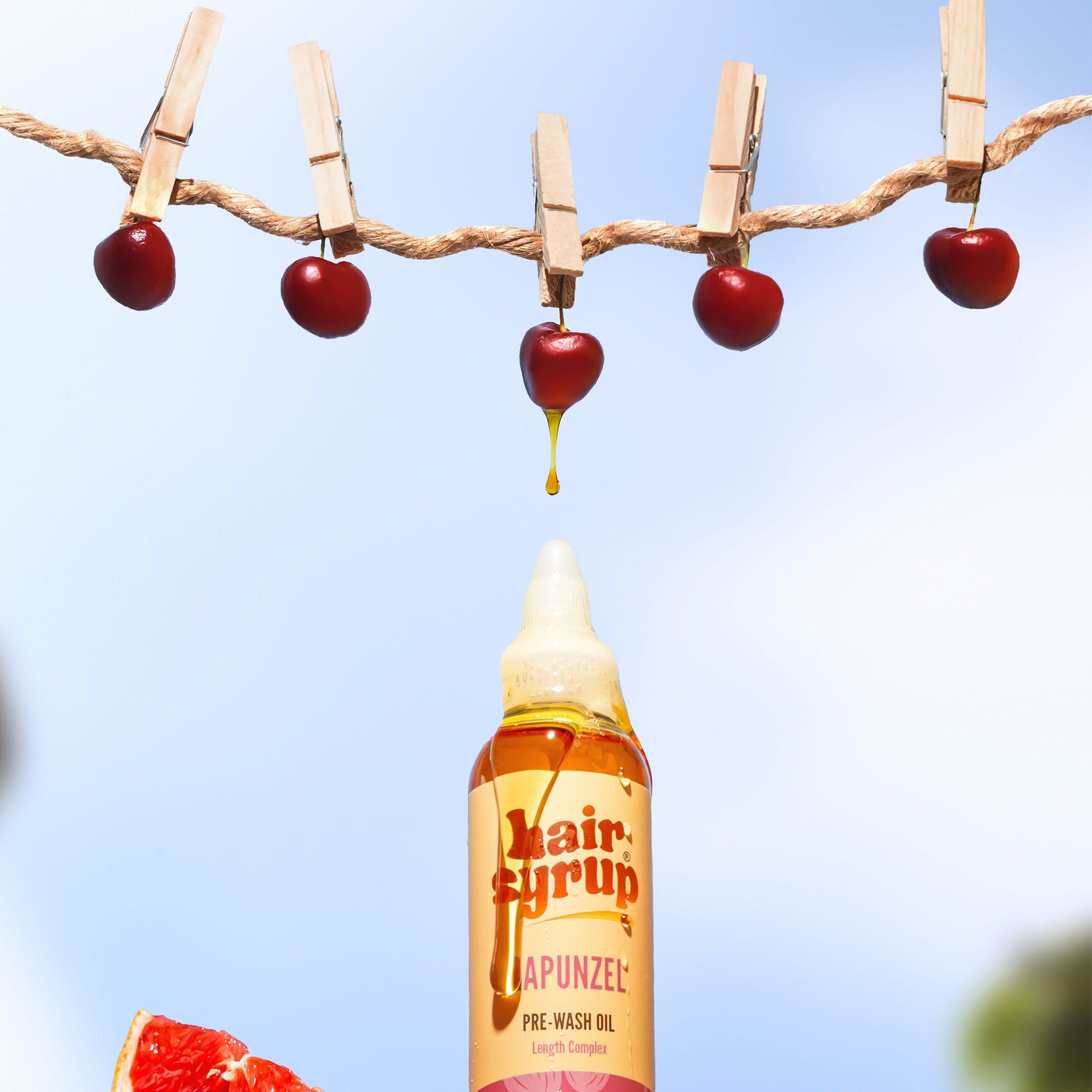 Hair Syrup Rapunzel Pre-Wash Oil-Flasche mit Kirschen an Wäscheklammern. Gelbe Flüssigkeit tropft.