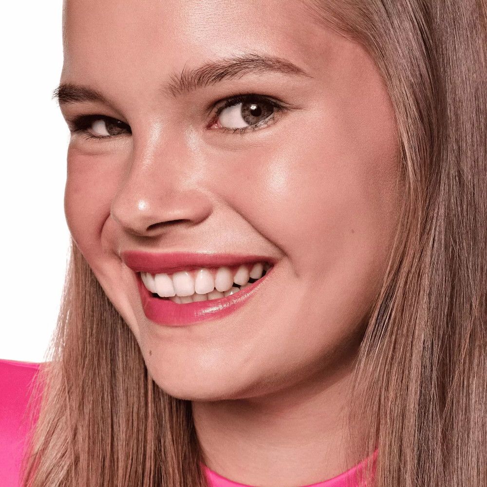 Porträt einer lächelnden Frau mit rosa Lippen. Sie trägt ein pinkfarbenes Oberteil.