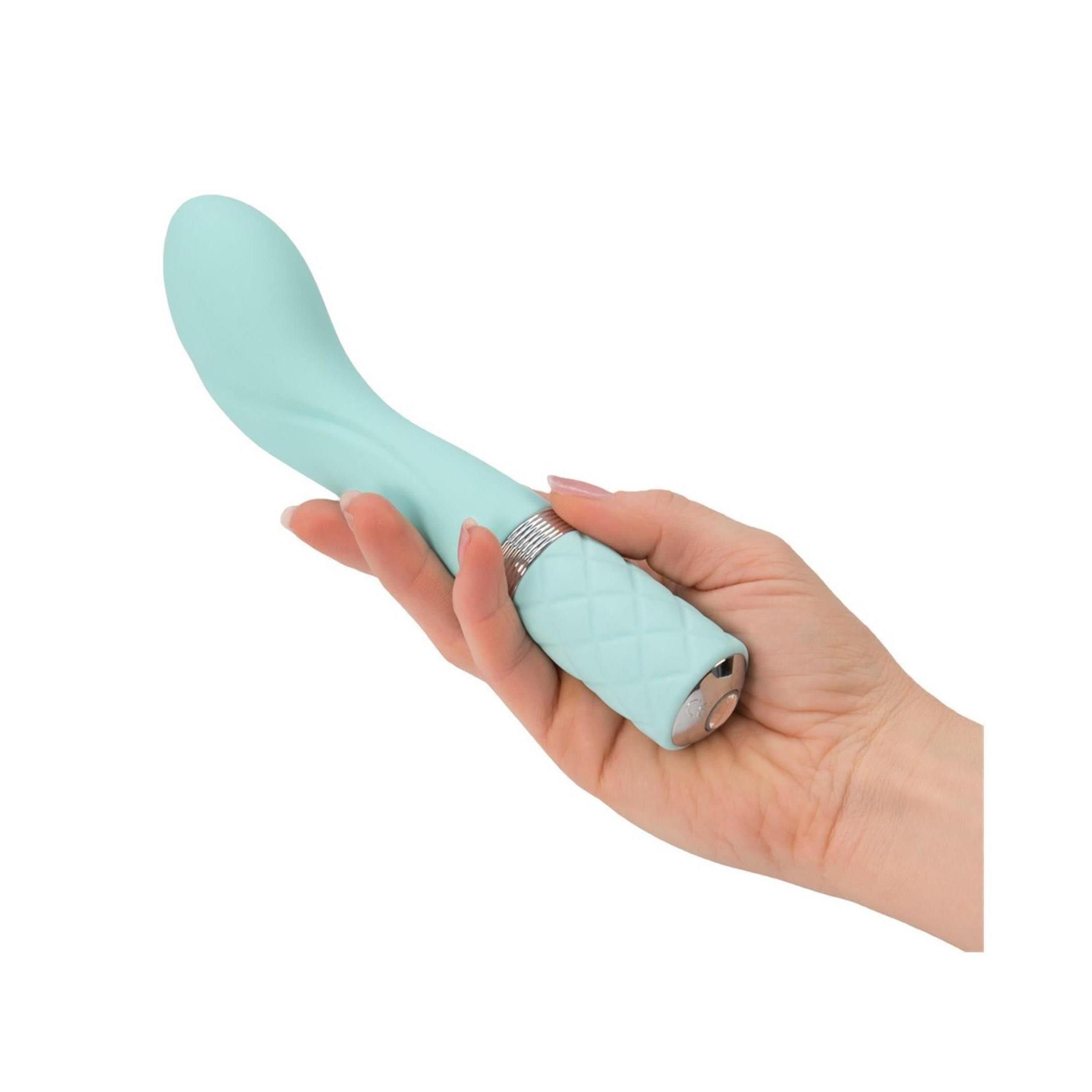 Hand hält türkisfarbenen Vibrator. Der Griff hat ein Rautenmuster. Silberfarbener Ring am Übergang.