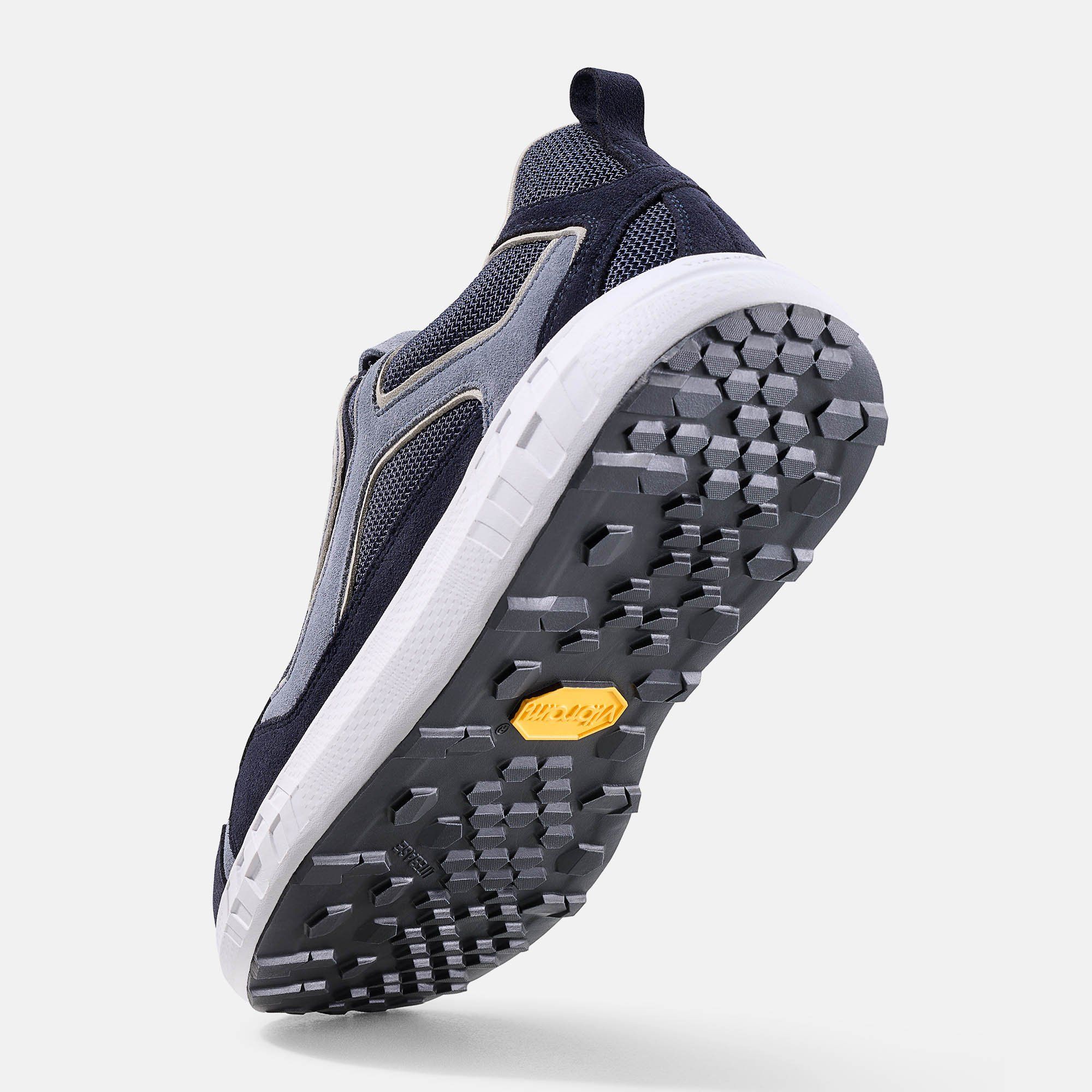 Unteransicht eines blauen Schuhs. Weiße Sohle, graue Details. Gelbes Vibram-Logo.