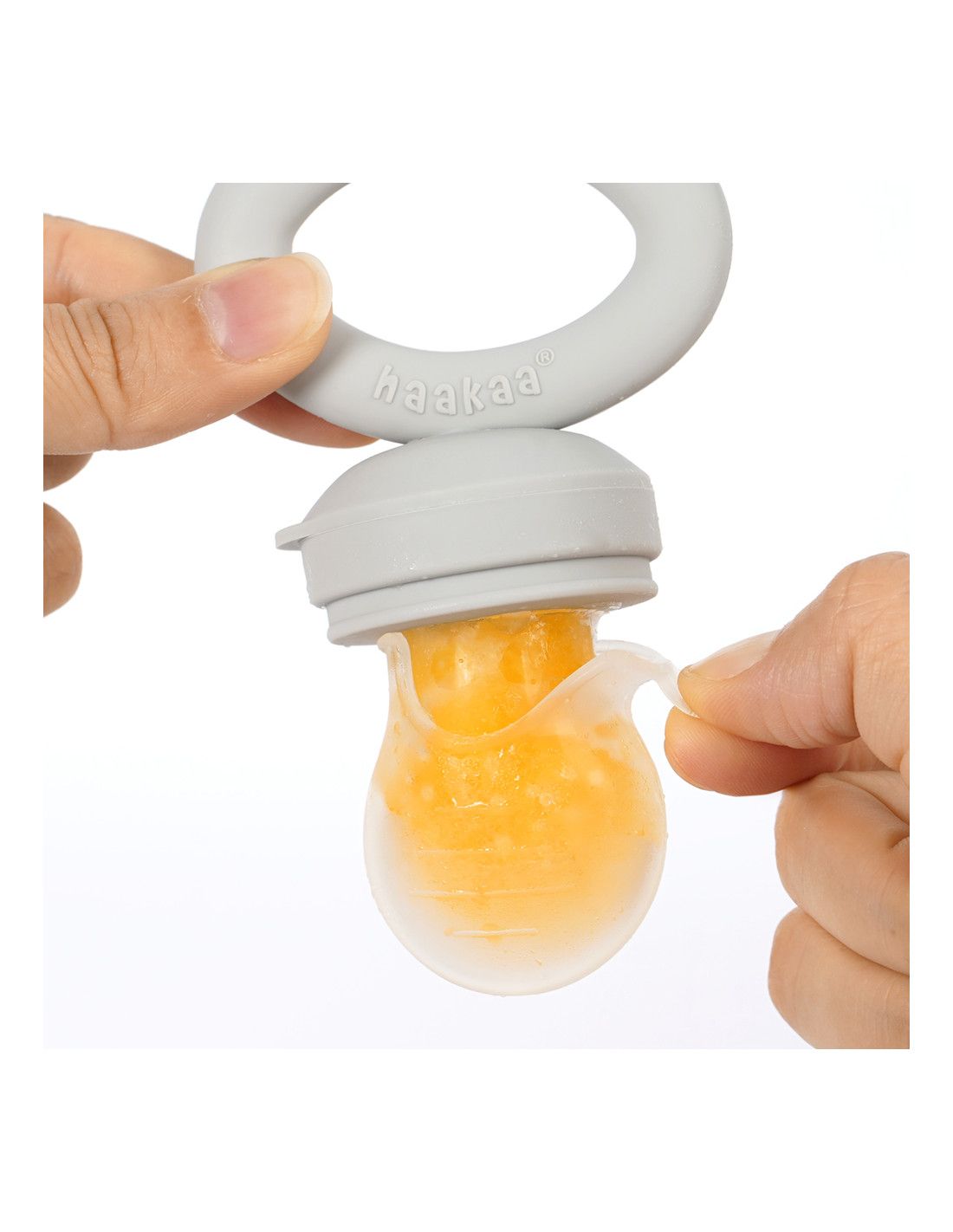 Grauer Fruchtsauger mit Fruchtfüllung. Ein Finger öffnet die transparente Schutzhülle. Der Sauger hat einen grauen Ring mit Logo.