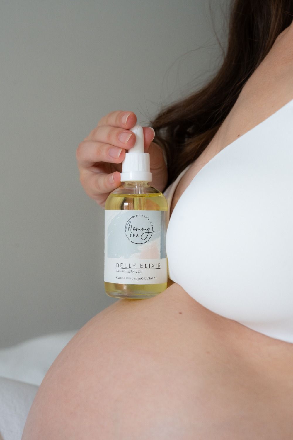 Schwangere Frau hält eine Flasche "Belly Elixir". Flasche mit Etikett "Mommy SPA".