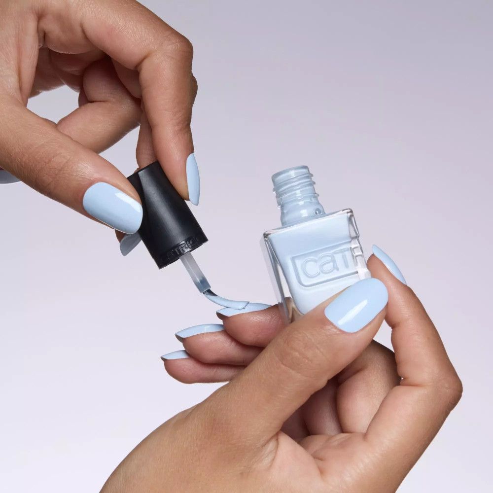 Hände halten eine Flasche hellblauen Nagellacks und tragen hellblauen Nagellack auf den Nägeln auf. Schwarzer Deckel.