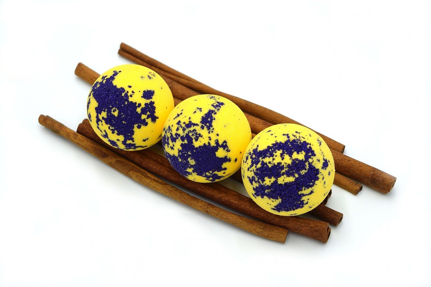 Drei gelbe, runde Badebomben mit blauen Flecken auf Zimtstangen. Auf weißem Hintergrund.