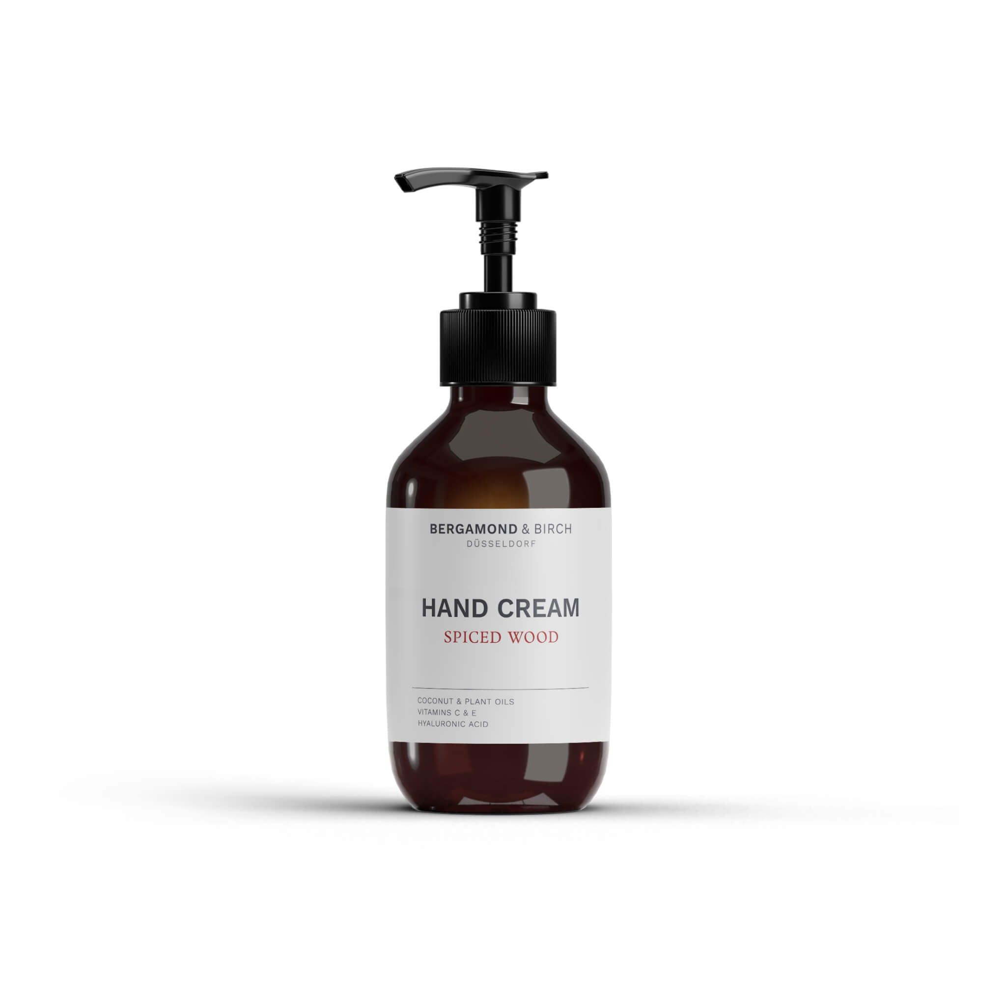 Braune Flasche mit schwarzem Pumpverschluss. Text: Hand Cream Spiced Wood. Aufschrift: BERGAMOND & BIRCH. Weißer Hintergrund.