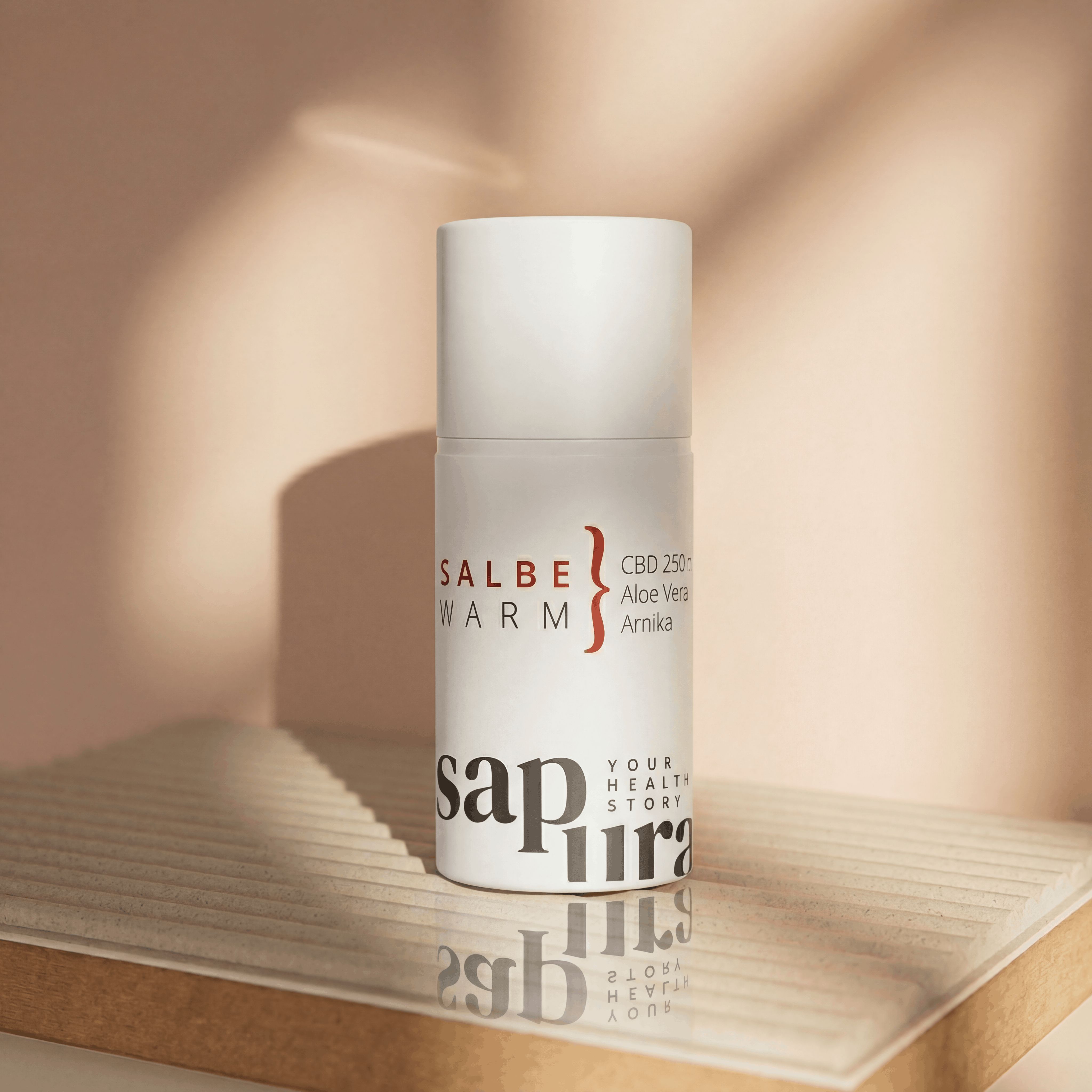 Weiße Pumpflasche mit "CBD SALBE WARM" und "CBD 250mg Aloe Vera Arnika" auf einer Holzablage.